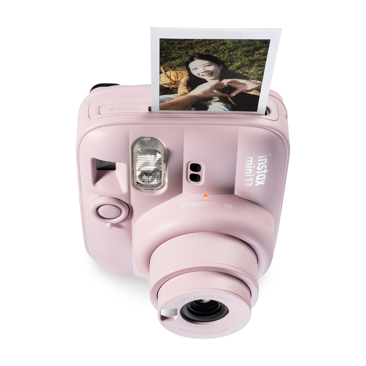Una fotocamera istantanea Instax Mini 13 rosa con una foto espulsa che mostra una donna sorridente.