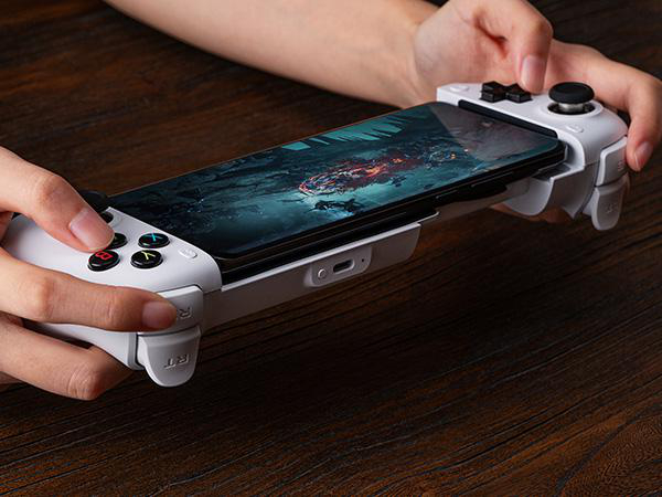 Person hält einen weißen mobilen Gamecontroller mit einem Smartphone auf einem Holz Tisch.