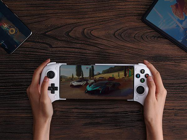 Hände halten einen weißen mobilen Gamecontroller mit einem Smartphone, auf dem ein Rennspiel läuft, auf Holzoberfläche.