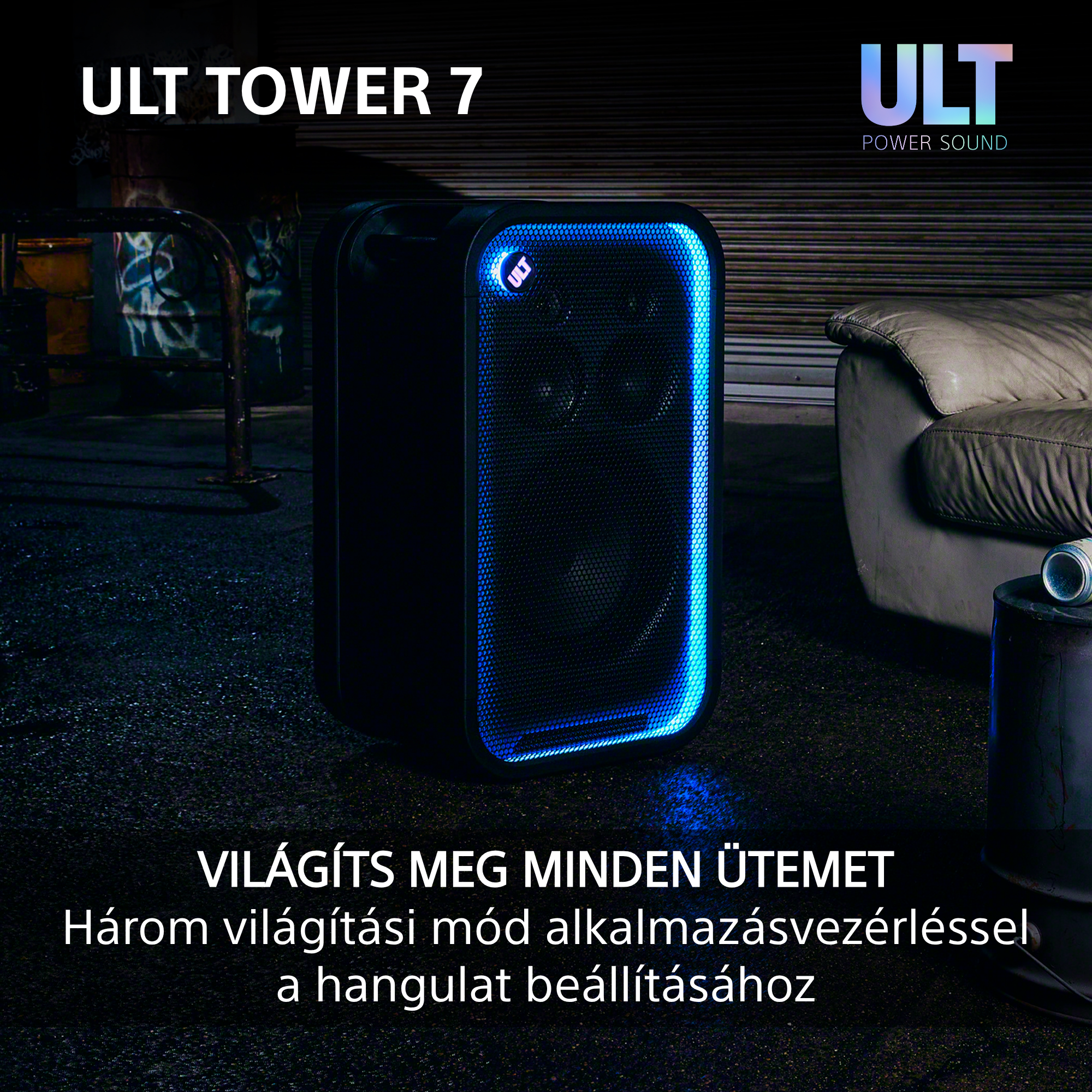 Fekete ULT Tower 7 hangszóró kék LED világítással egy sötét szobában, kanapéval.