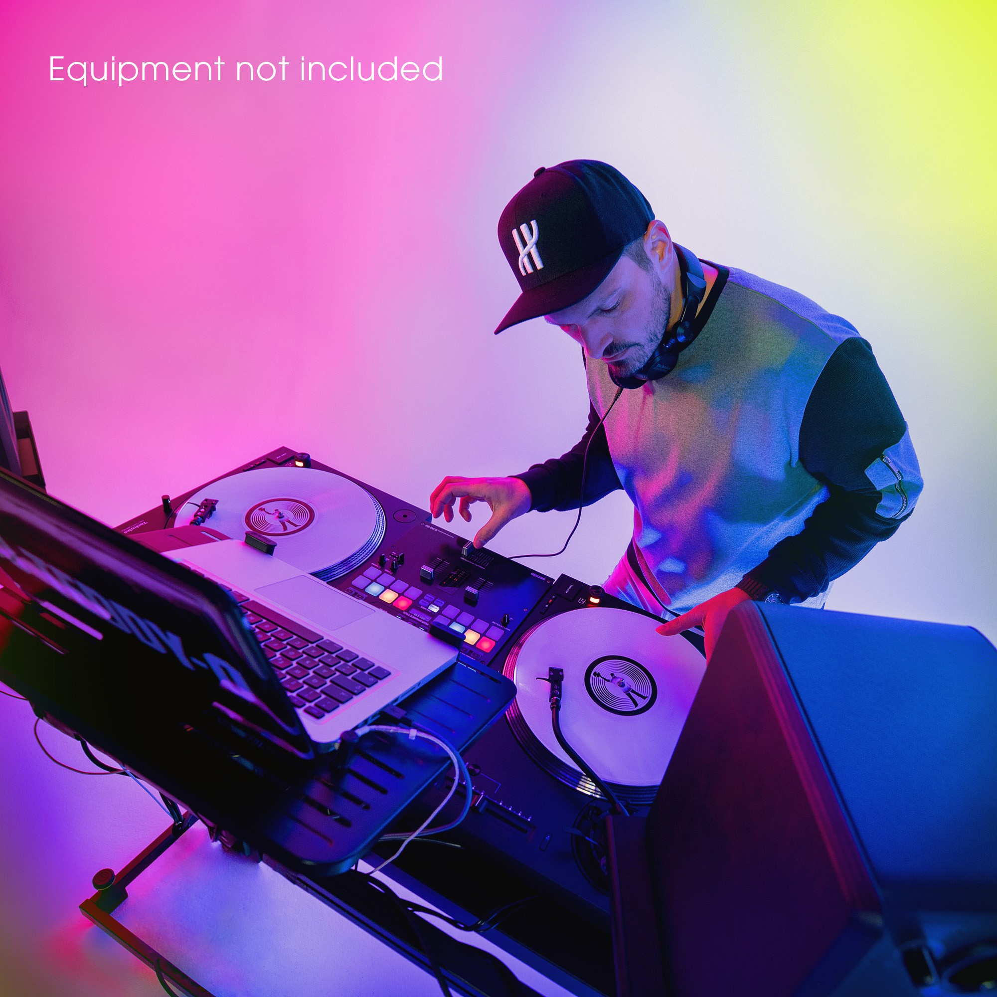 Un DJ casquette mixe de la musique sur une table de mixage avec platines et ordinateur portable.