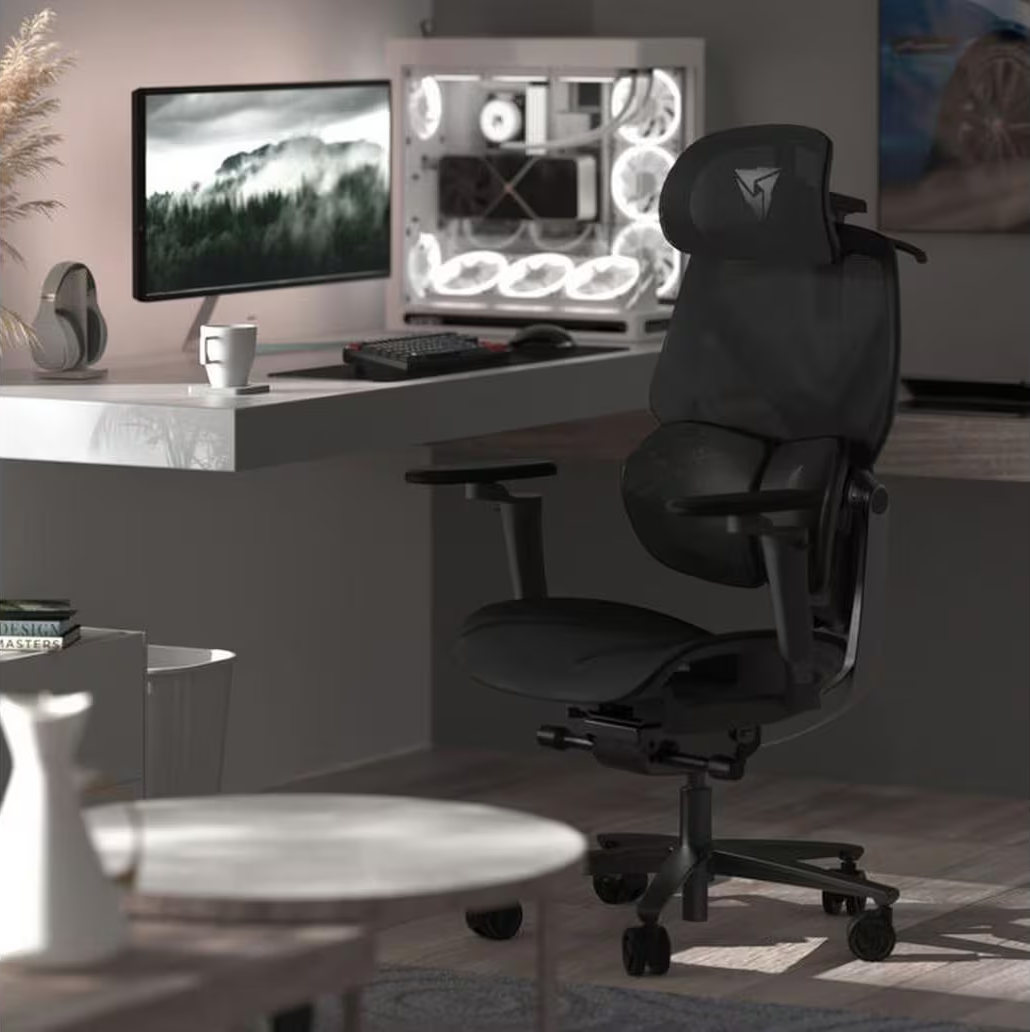 Una sedia da ufficio ergonomica nera davanti a una scrivania con PC, monitor e tazza.