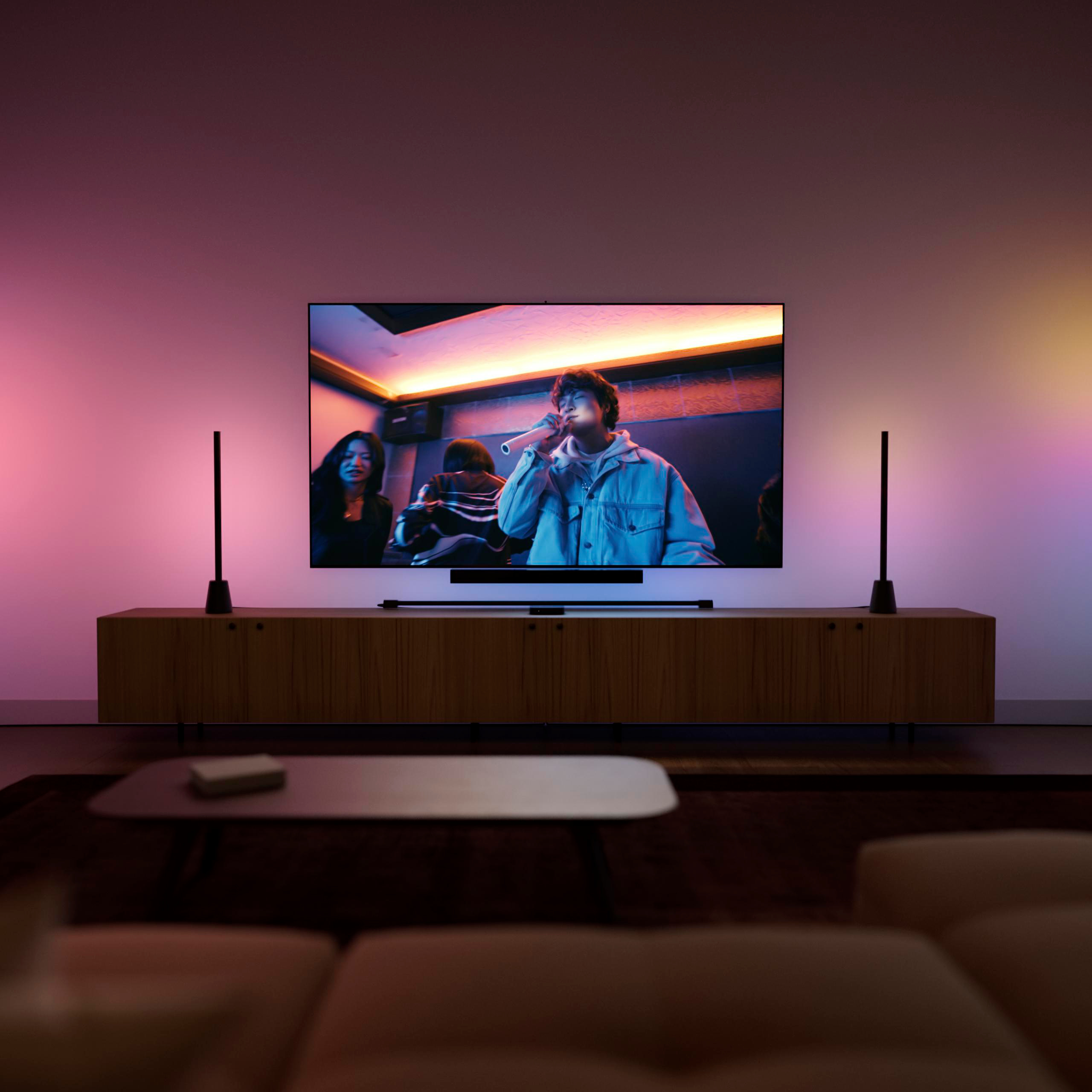 Wohnzimmer mit TV auf Schrank, stimmungsvoller Hintergrundbeleuchtung und Sofas im Vordergrund.