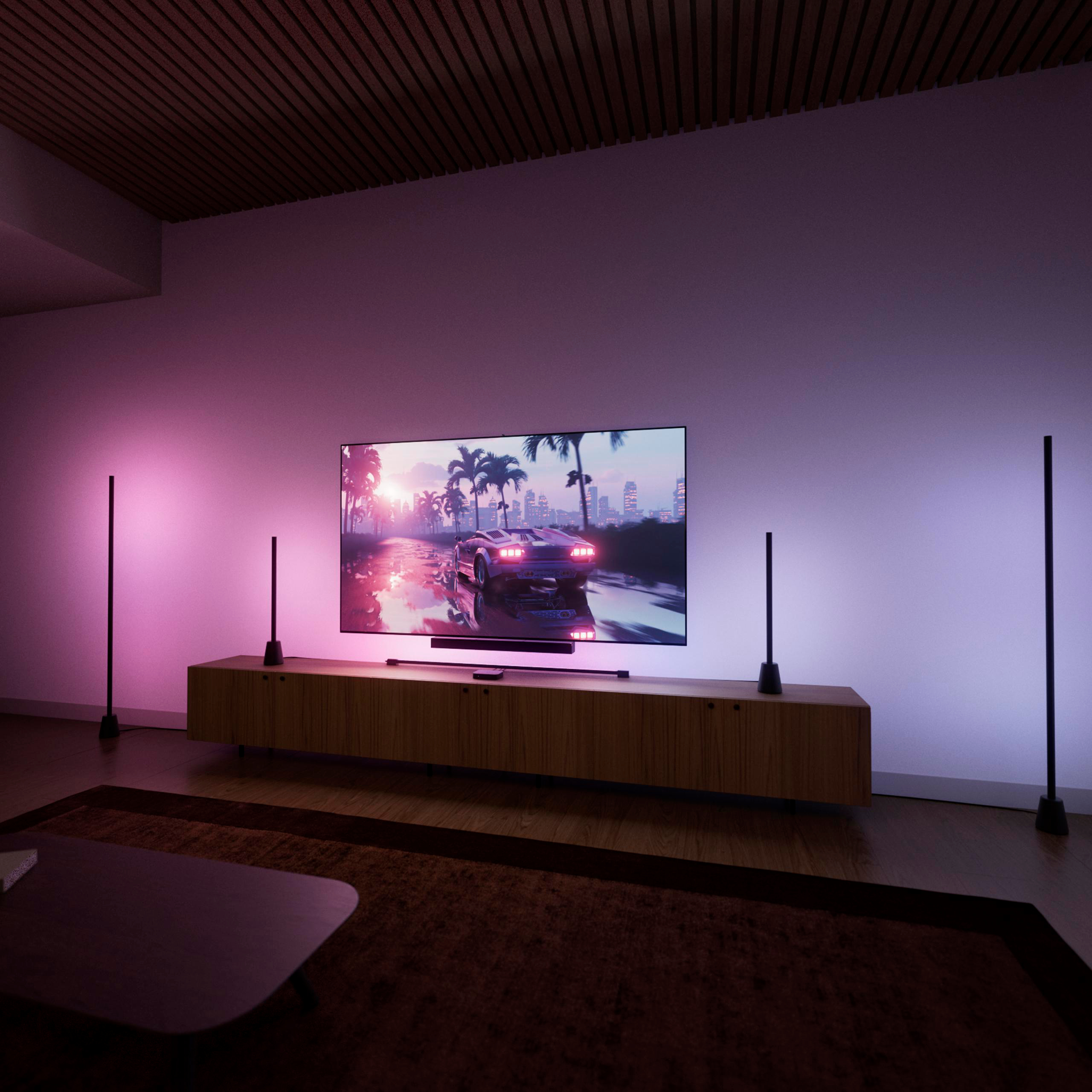 Ein Wohnzimmer mit TV auf einem Holzschrank, umgeben von stimmungsvoller rosa Beleuchtung und Stehlampen.