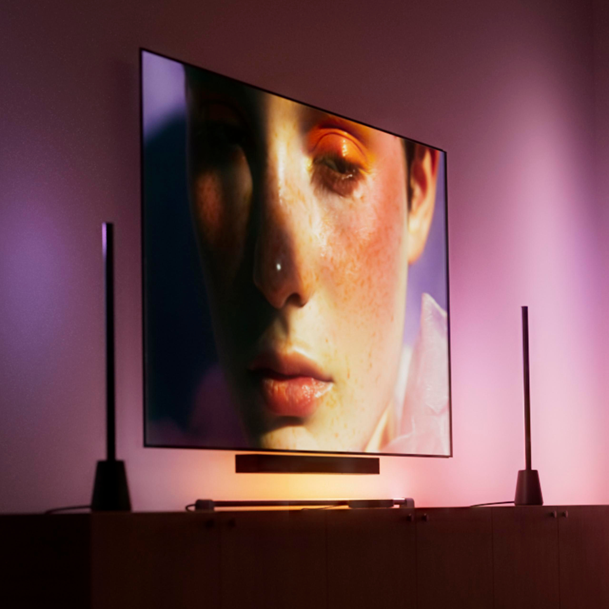 Ein Flachbildfernseher zeigt ein Gesicht, montiert an einer Wand mit Umgebungslicht und Lautsprechern.