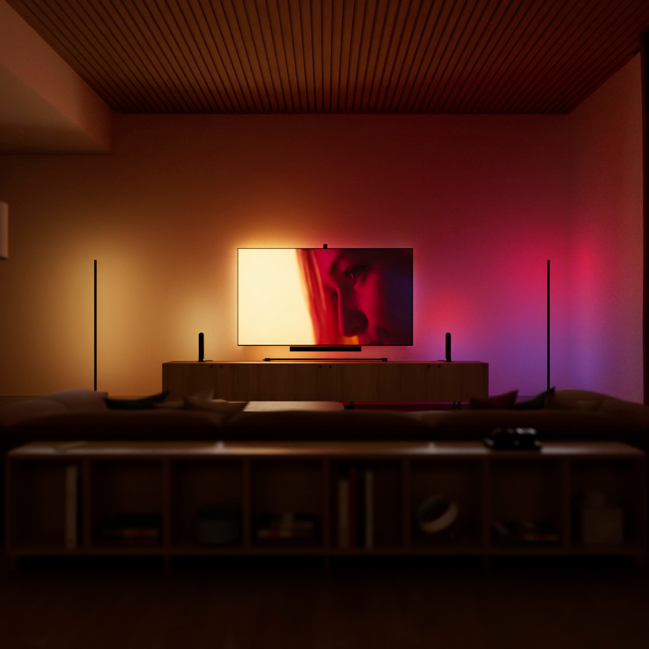 Wohnzimmer mit flachem Fernseher, Stimmungsbeleuchtung und Regalen im Vorder- und Hintergrund.