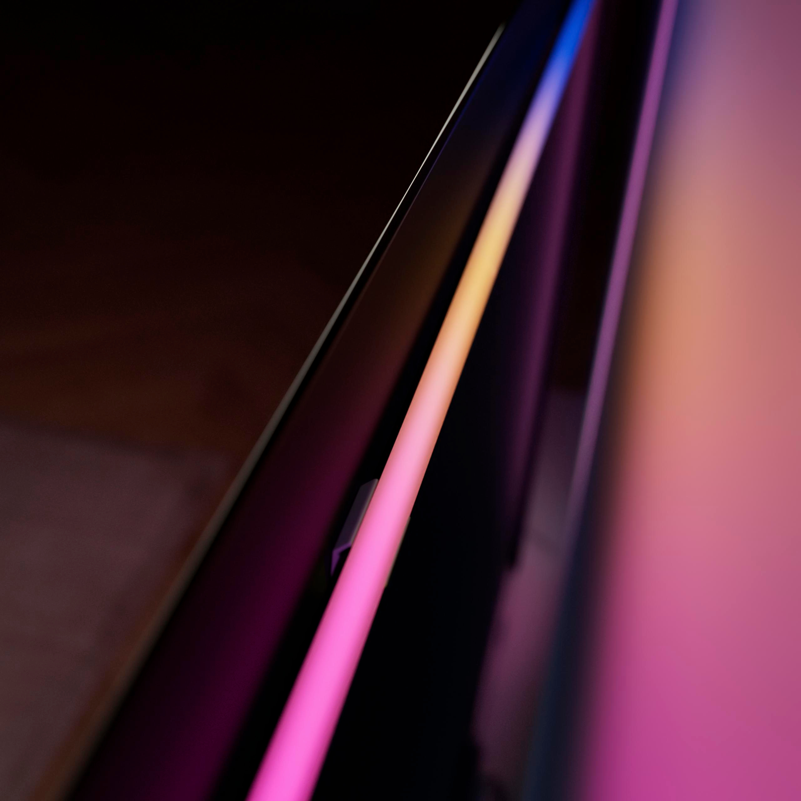 Eine Nahaufnahme zeigt eine schlanke LED-Lichtleiste mit leuchtend rosa und orangem Licht an einer Wand.