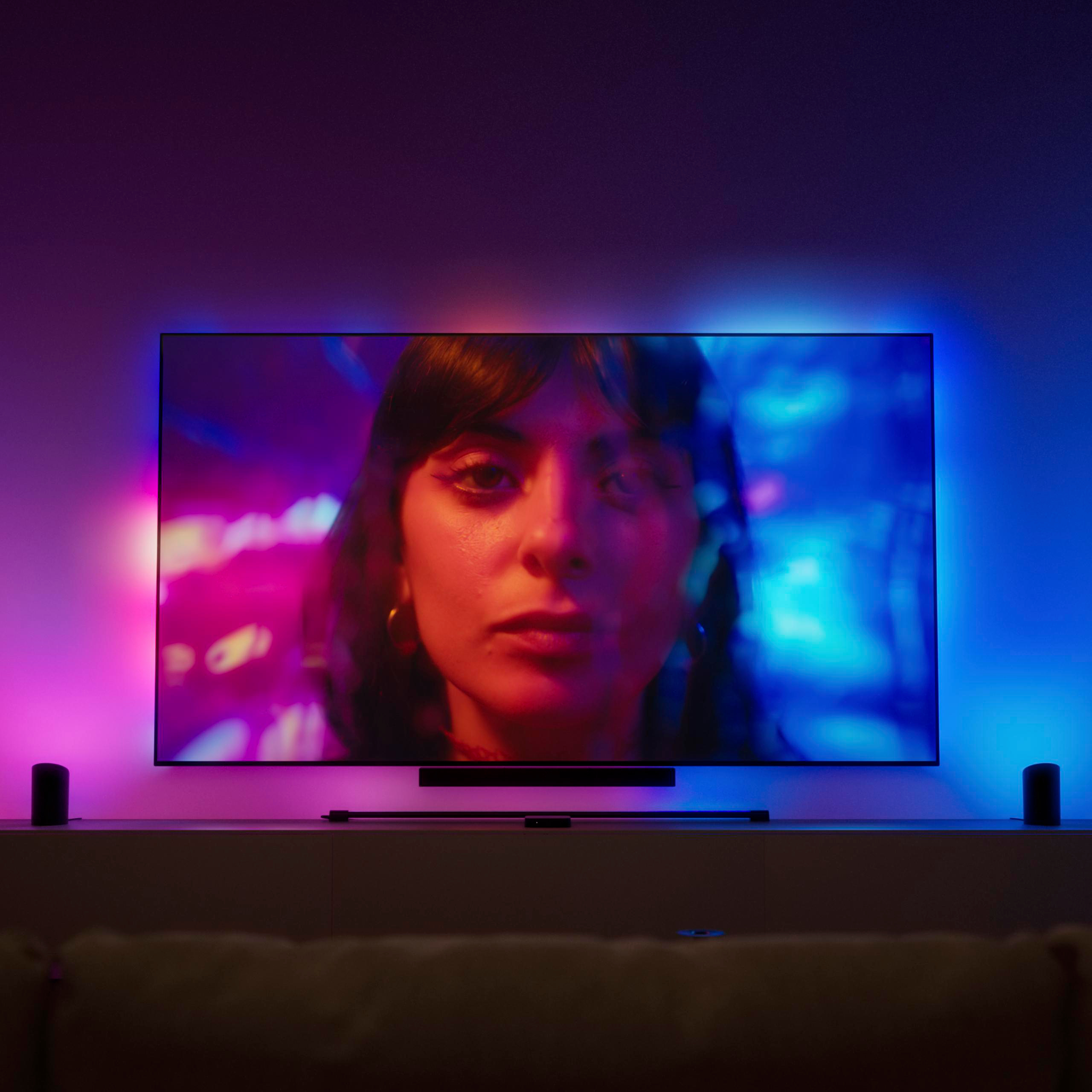 Ein Fernseher zeigt das Gesicht einer Frau, umgeben von leuchtender blauer und rosa Hintergrundbeleuchtung.