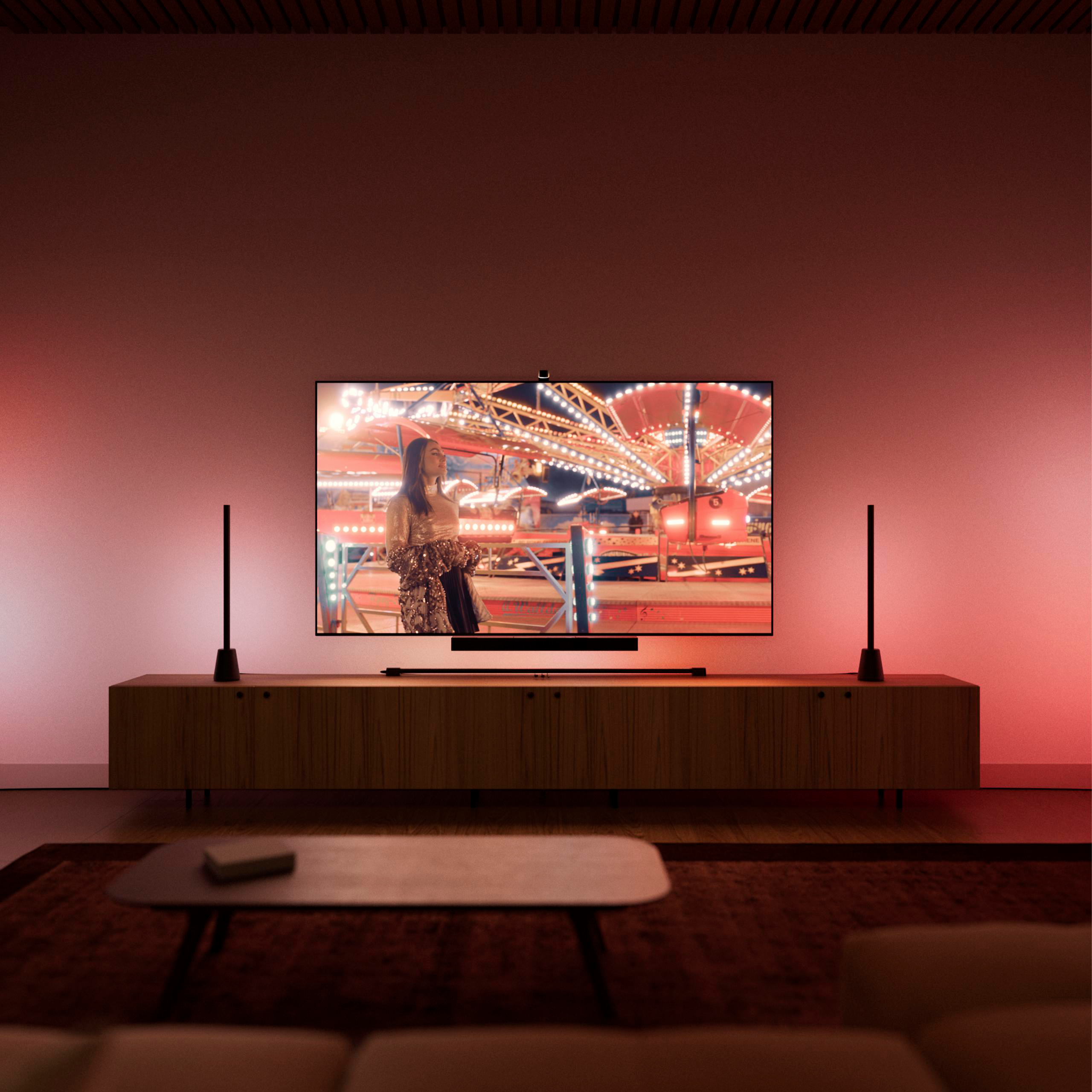 Wohnzimmer mit TV auf Sideboard, das eine Frau vor einem Jahrmarkt zeigt. Rote Hintergrundbeleuchtung.