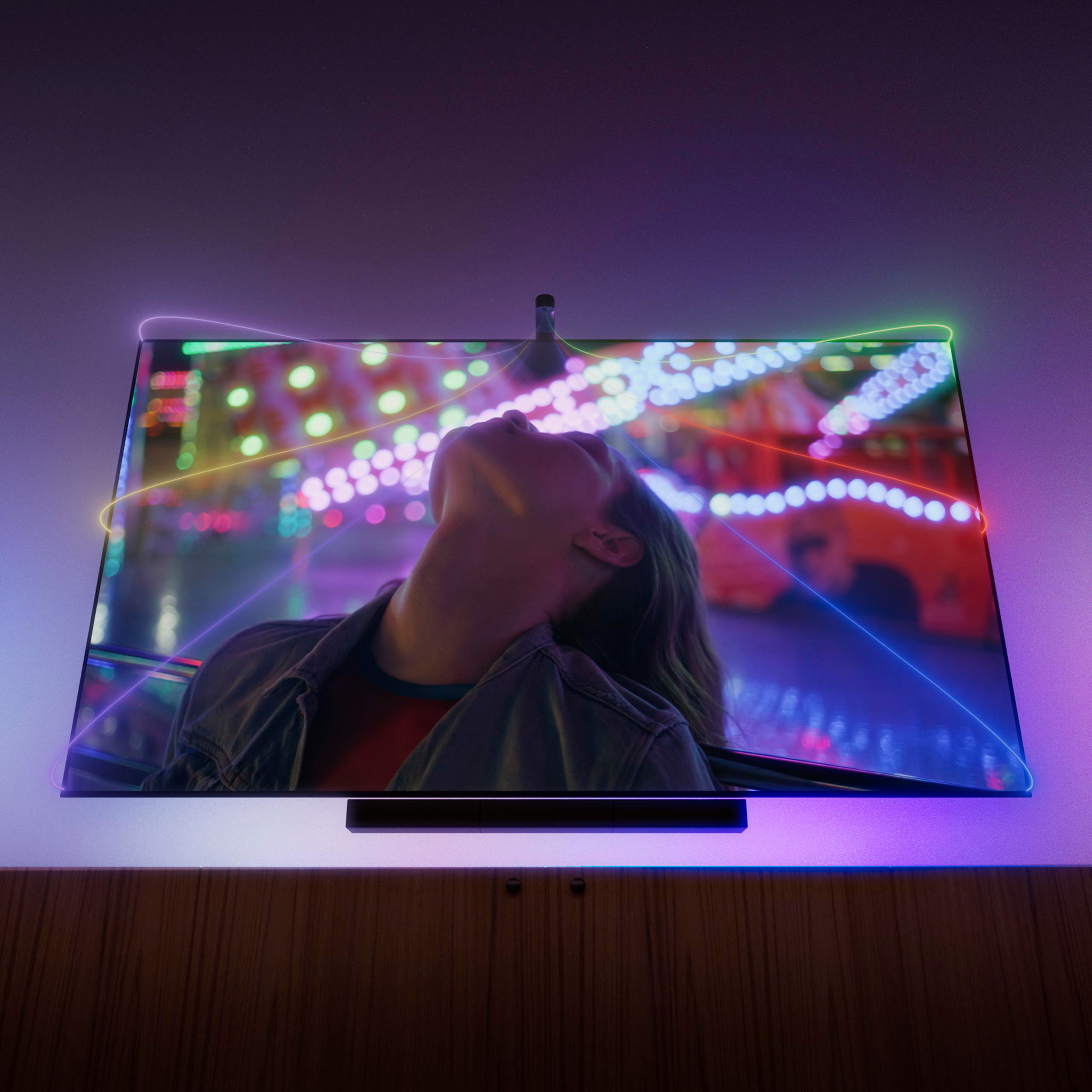 Ein Fernseher zeigt eine Frau, die nach oben blickt, umgeben von bunten Lichtern und Laserstrahlen.