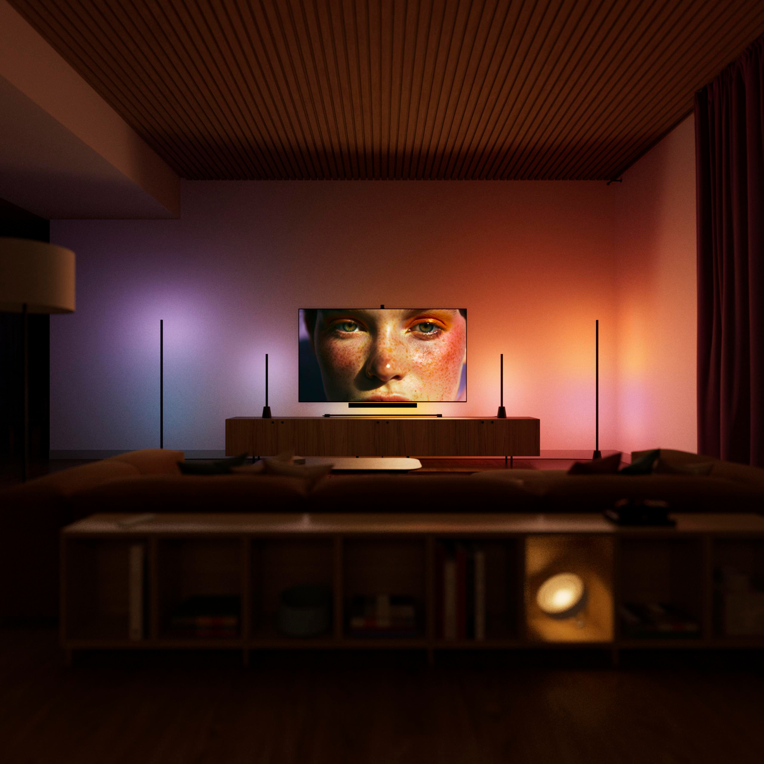 Gemütliches Wohnzimmer mit TV, der ein Frauengesicht zeigt, flankiert von farbigen Ambientelampen und Holzelementen.