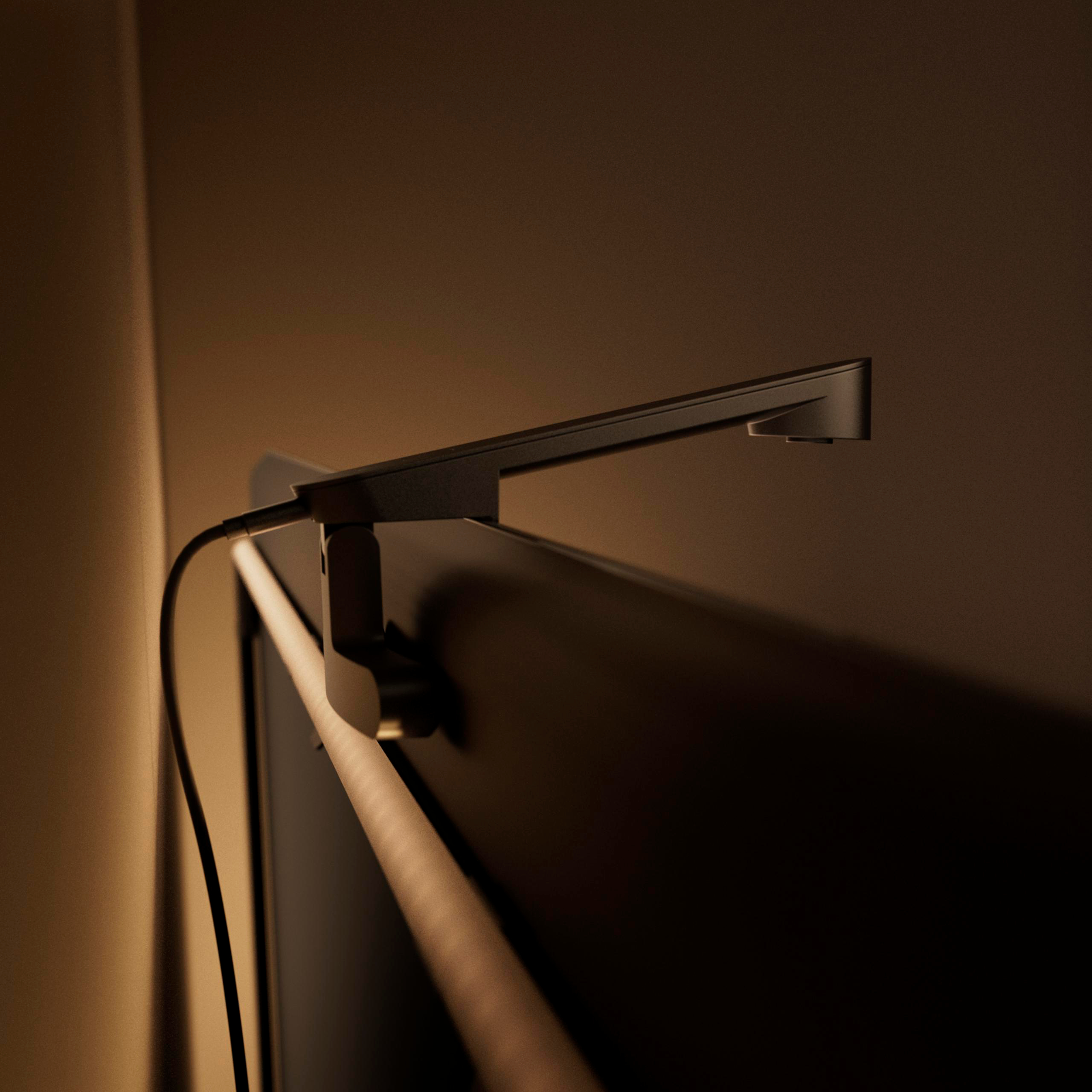 Eine elegante Bildschirm-Leuchte ist auf einem Monitor montiert und wirft ein warmes Licht an eine schlichte Wand.