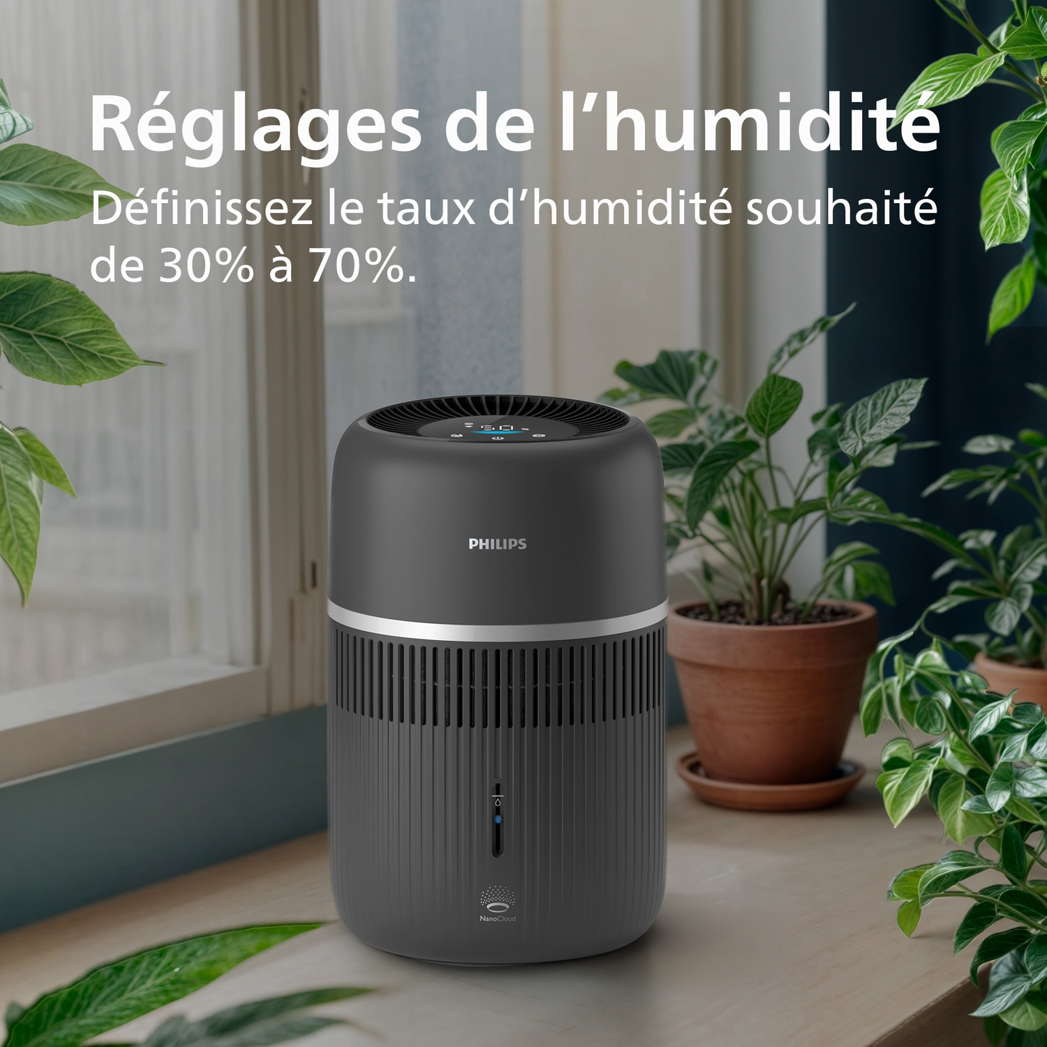 Humidificateur Philips gris sur une surface en bois avec des plantes vertes en arrière-plan.