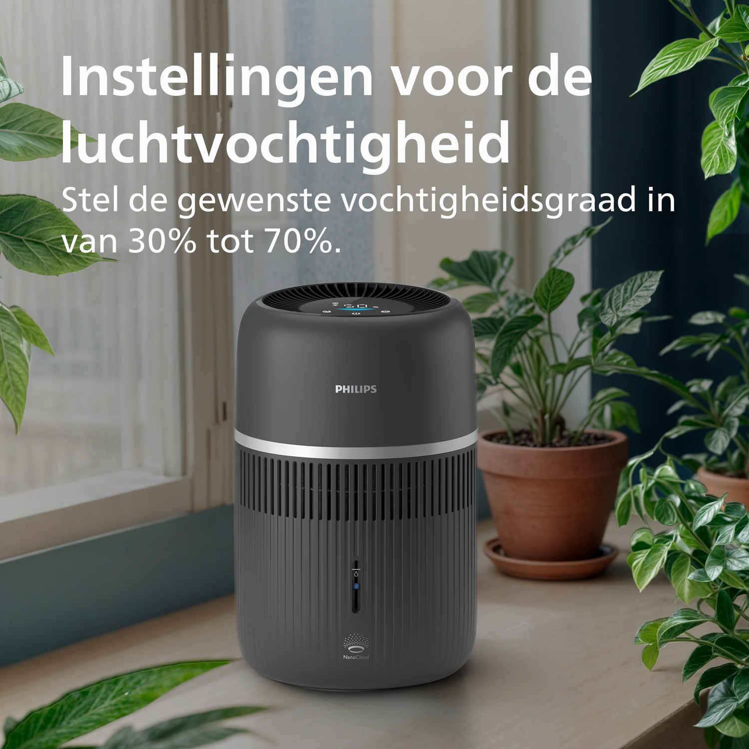 Een grijze Philips luchtbevochtiger staat op een tafel voor een raam, omringd door groene potplanten.