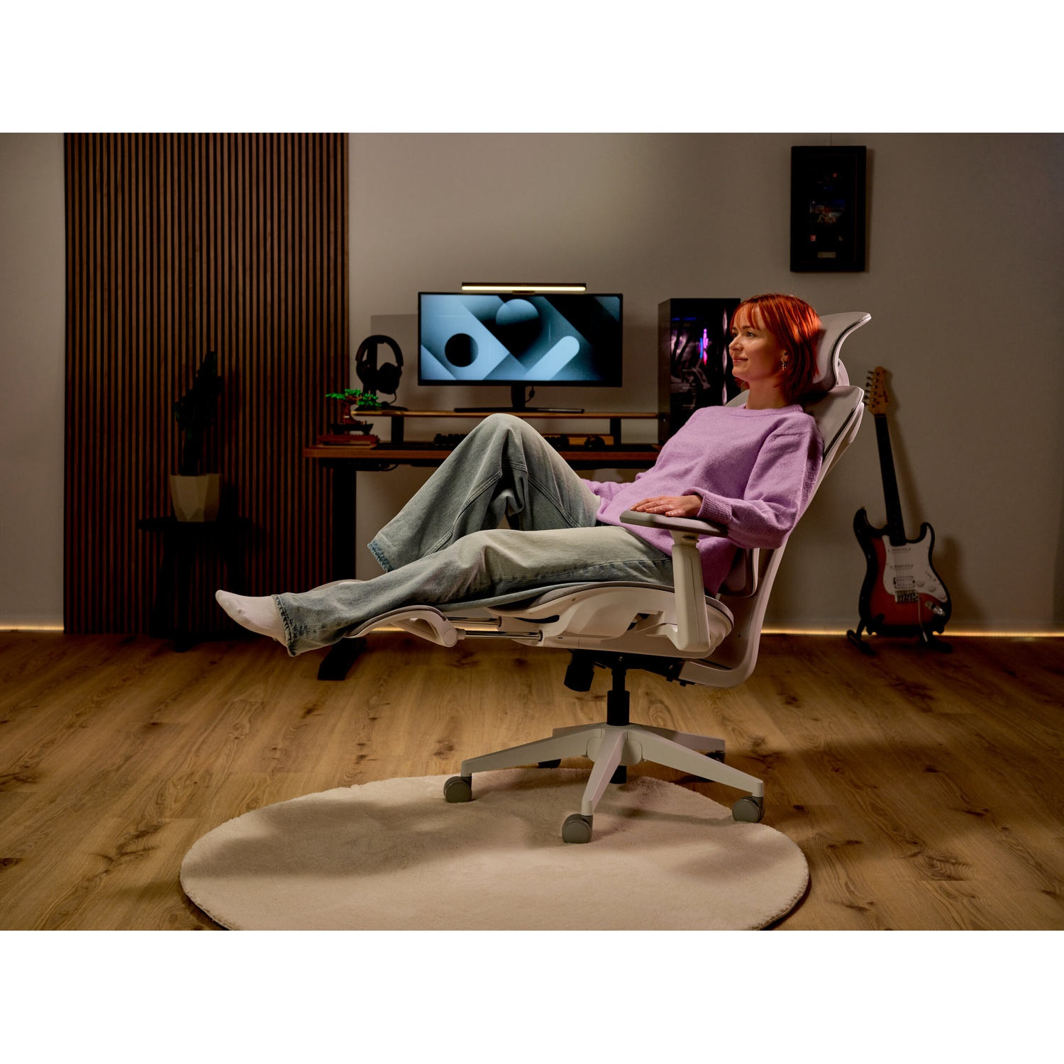 Una donna dai capelli rossi con un maglione viola si rilassa su una sedia da ufficio ergonomica.