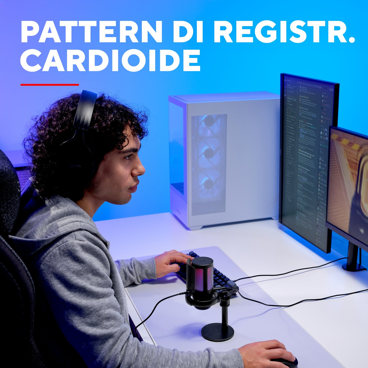 Un giovane con le cuffie siede a una scrivania davanti ai computer, digitando su una tastiera.