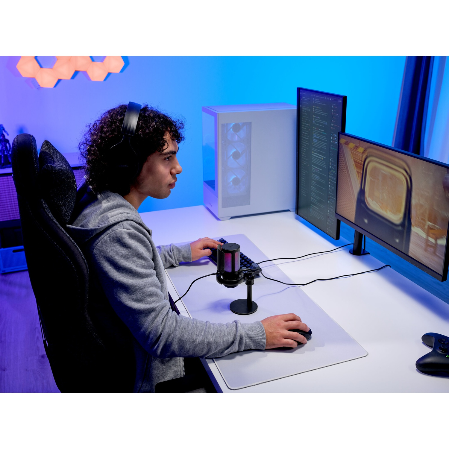 Un giovane con le cuffie gioca a una scrivania con due monitor in una stanza illuminata di blu.