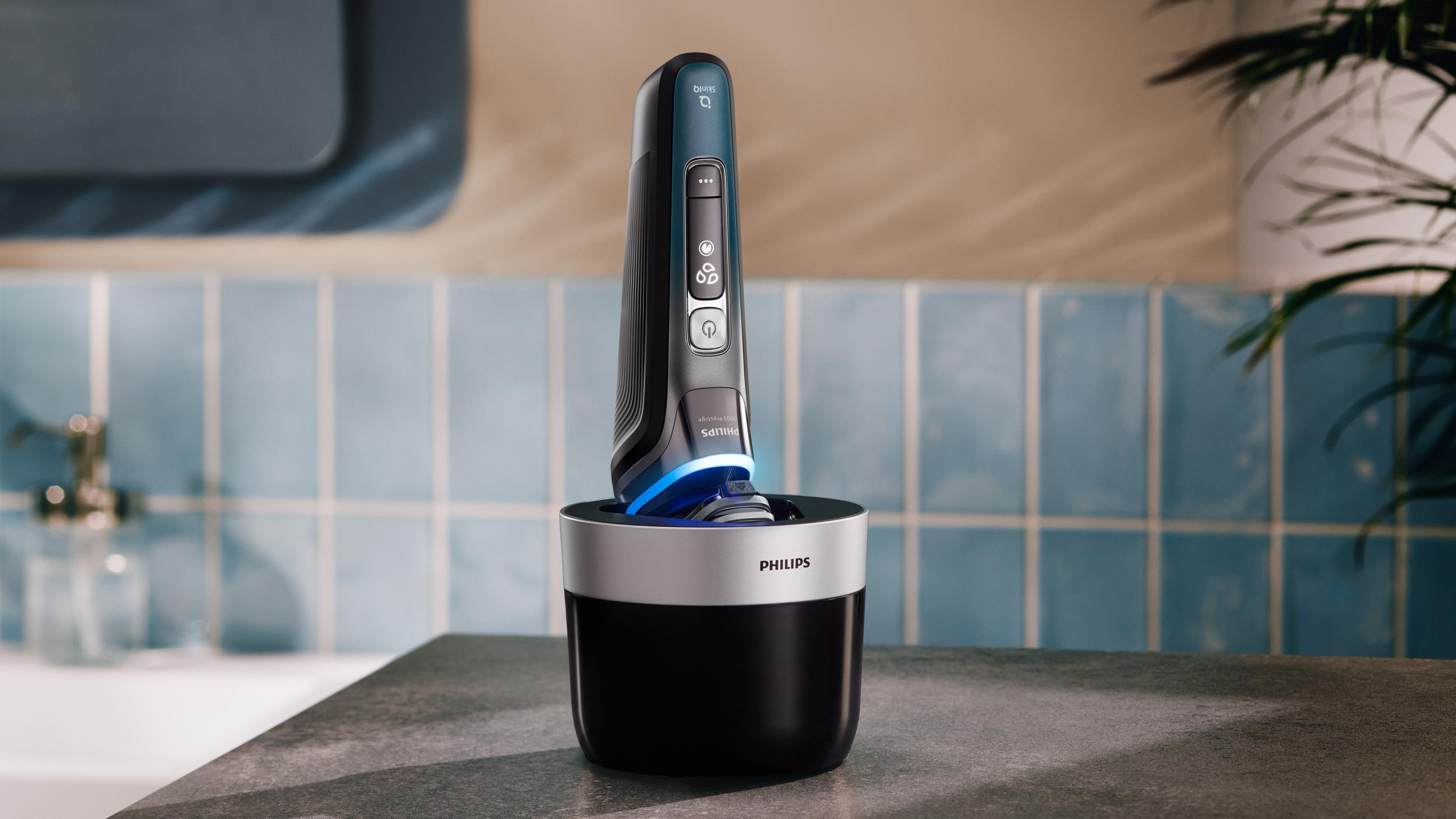 Ein schwarzer Philips Rasierer steht in einer Ladestation auf einer grauen Oberfläche vor blauen Fliesen.