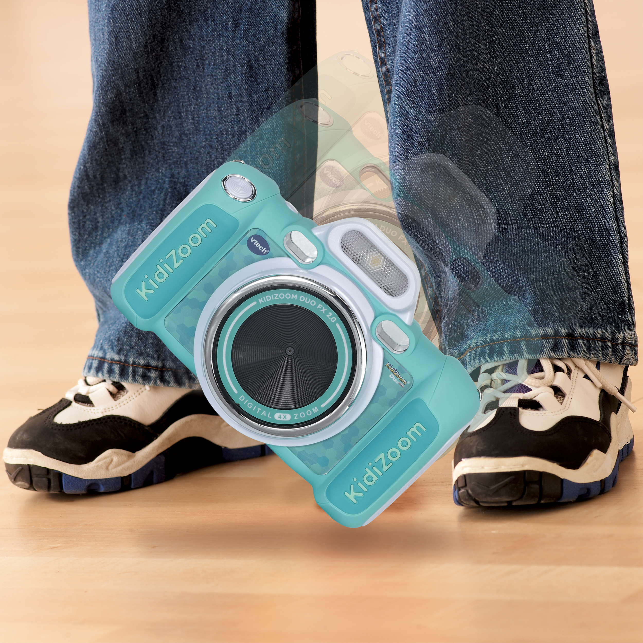 Eine türkisfarbene VTech KidiZoom Kamera schwebt vor einer Person in Jeans und Sneakers.