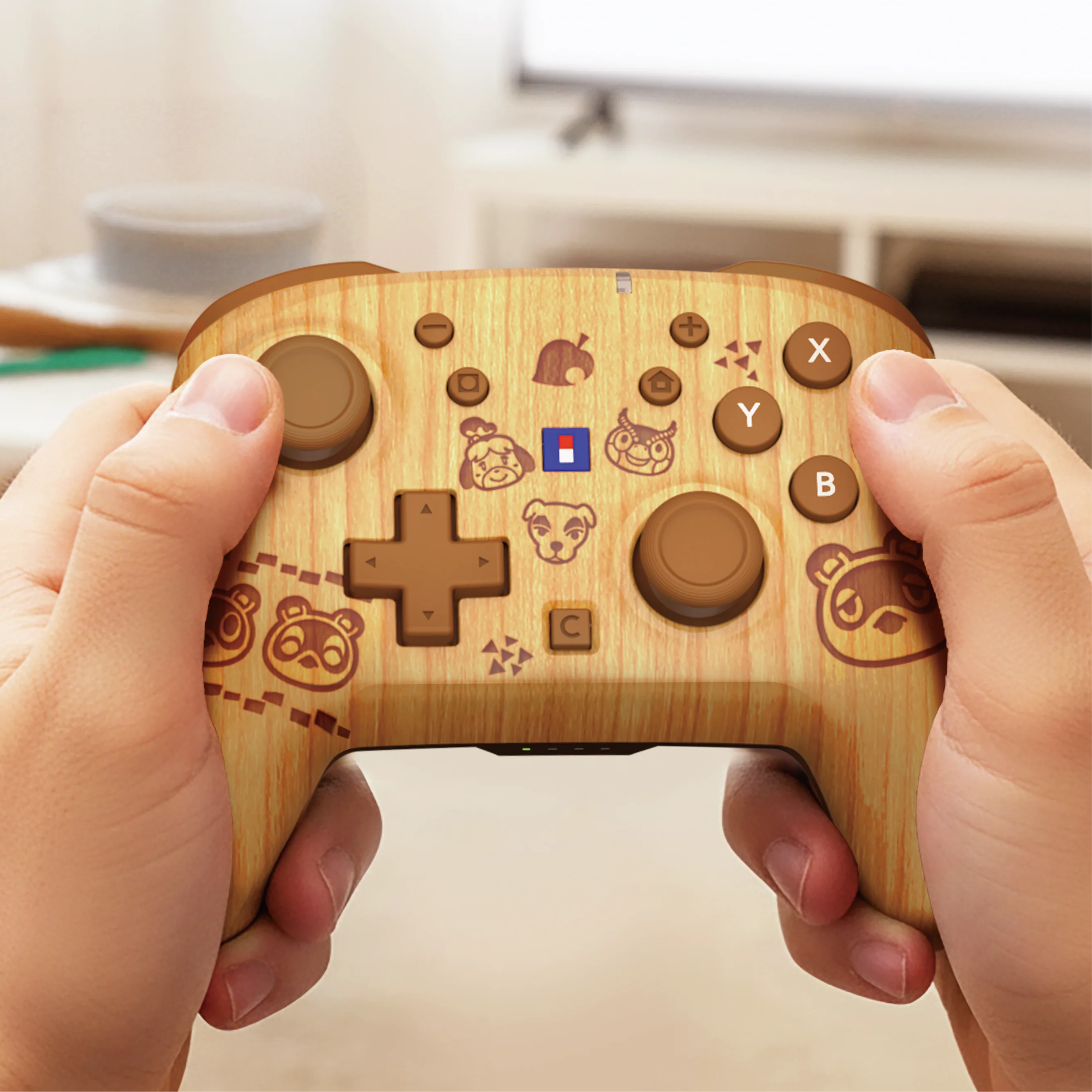 Ein holzfarbener Animal Crossing Gamepad wird von zwei Händen in einem hellen Zimmer gehalten.