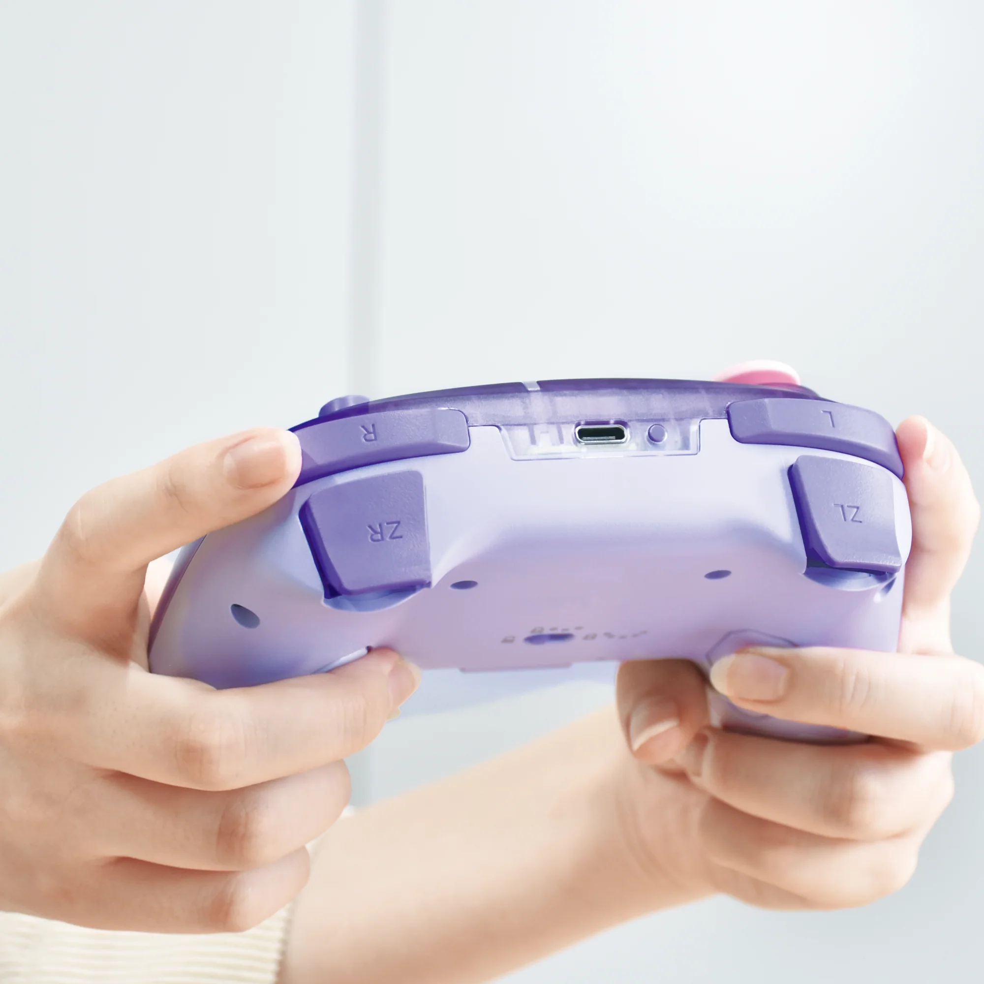 Hände halten einen hellvioletten Videospiel-Controller mit USB-C-Anschluss.