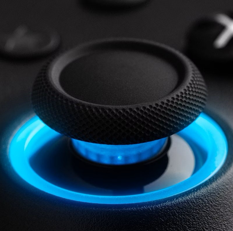 Un joystick per gamepad nero circondato da un anello LED blu luminoso su sfondo scuro.