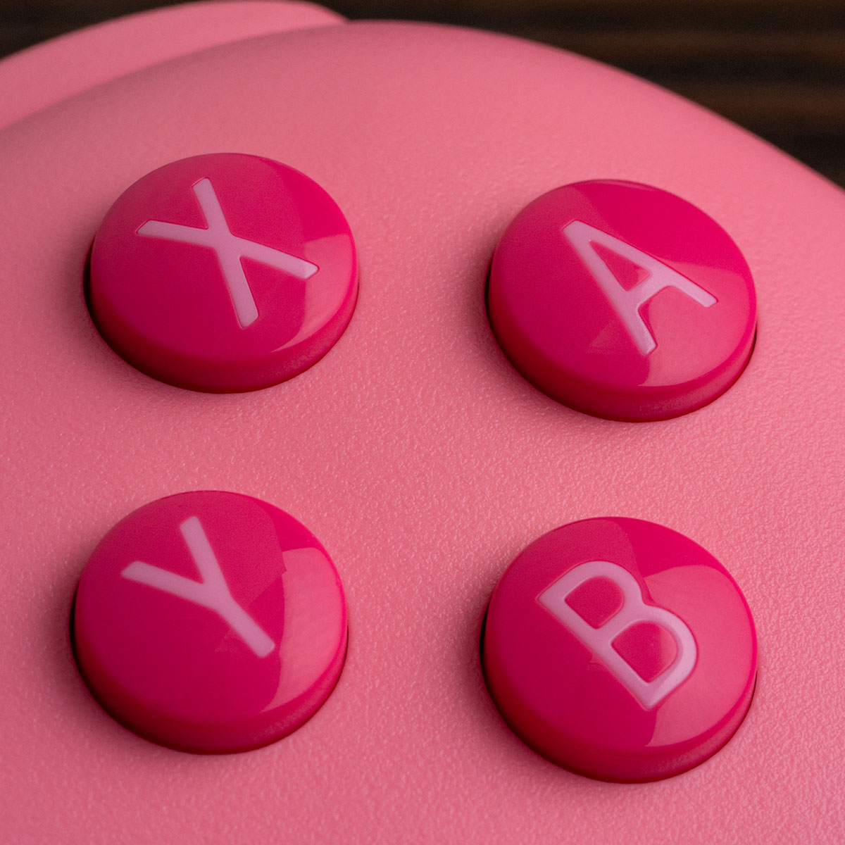 Nahaufnahme von vier runden, pinken Gaming-Controller-Tasten mit den Buchstaben X, A, Y und B auf pinkem Hintergrund.