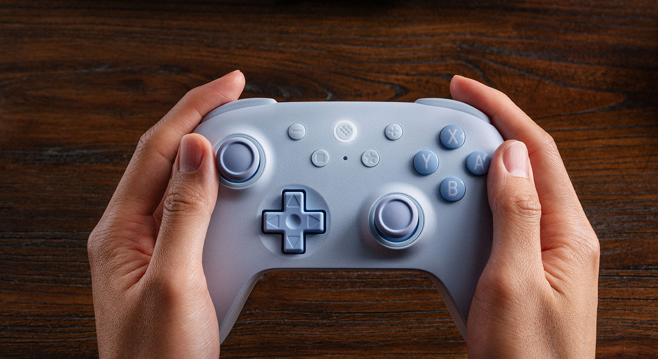 Hände halten einen hellblauen Gamecontroller vor einem Holzhintergrund.