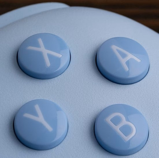 Vier blaue Tasten mit weißen Buchstaben X, A, Y, B auf einem hellblauen Controller.