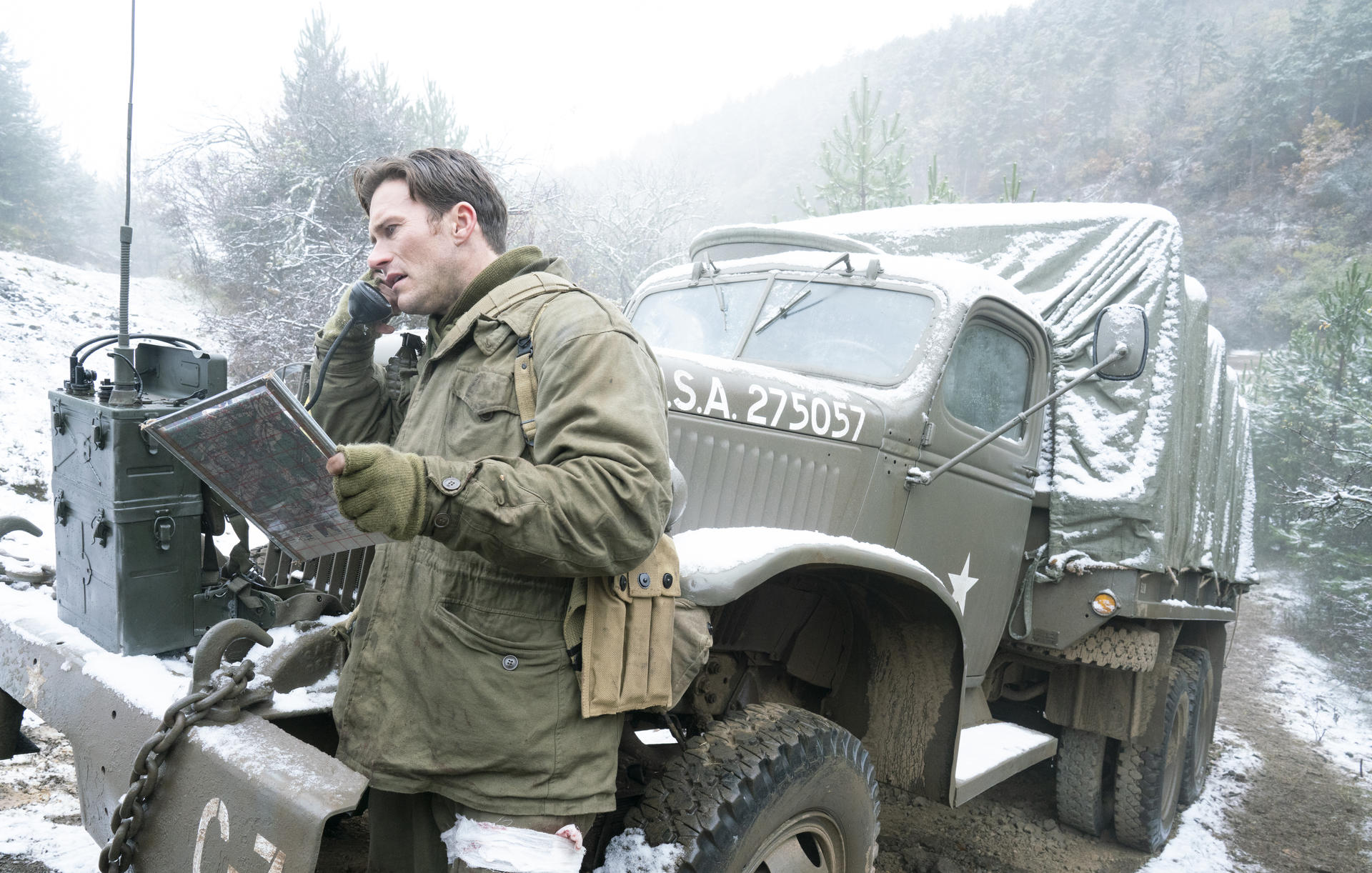 Ein Soldat in Winterkleidung telefoniert vor einem Militärlastwagen mit einer Karte.
