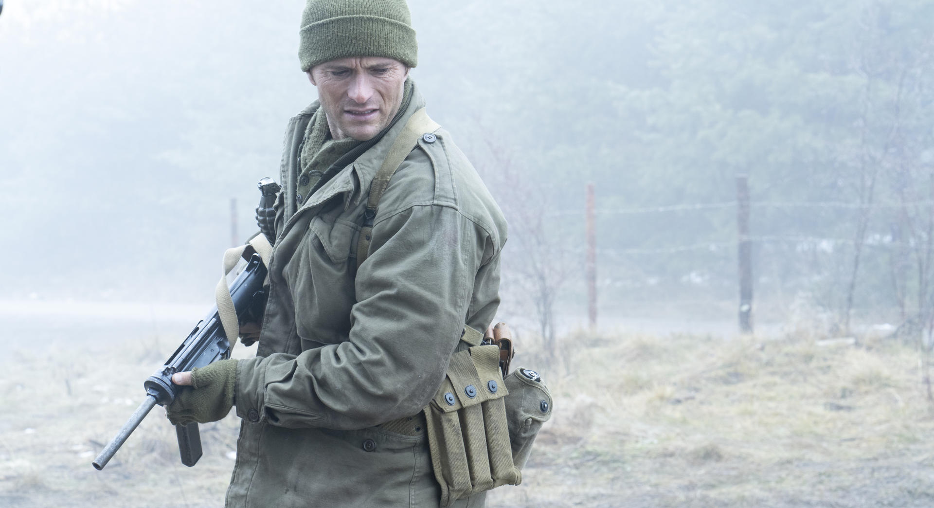 Ein Soldat in grüner Winterkleidung und Mütze hält ein Gewehr im Nebel.
