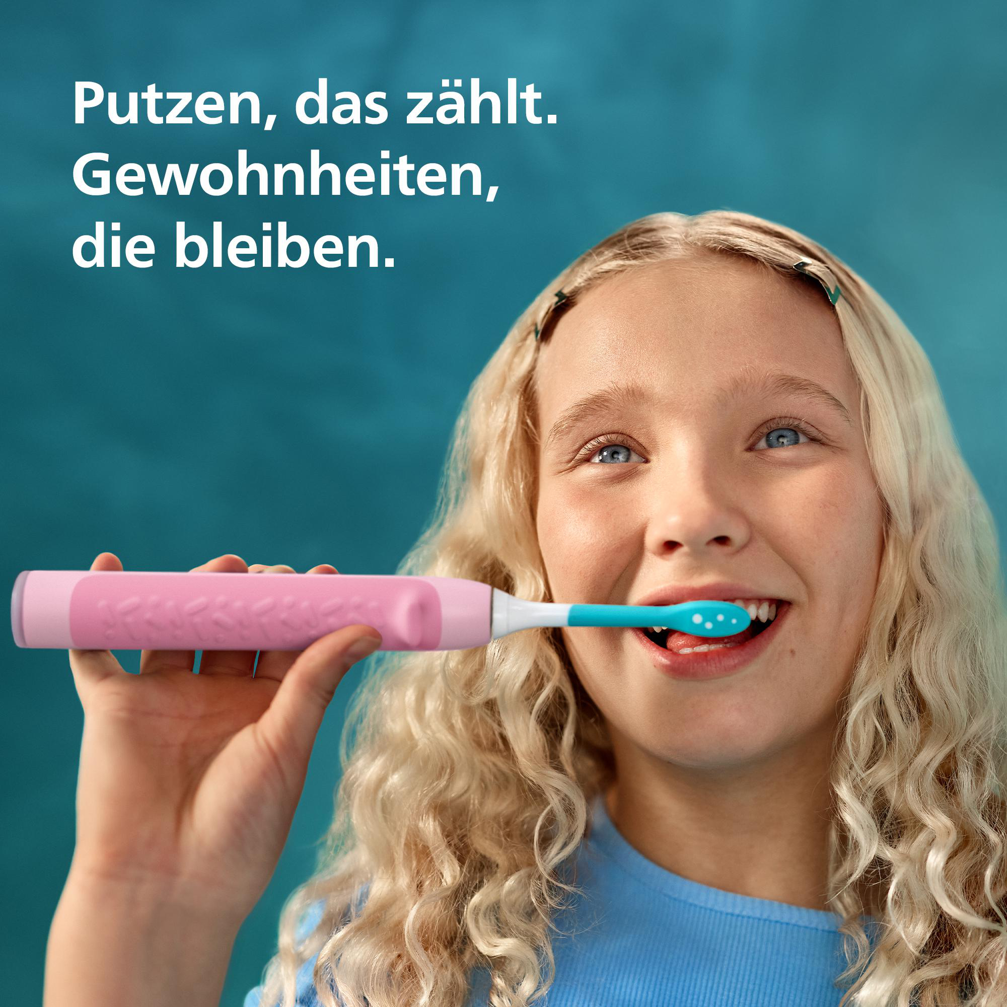 Ein blondes Mädchen lächelt und putzt sich mit einer pinken elektrischen Zahnbürste die Zähne.
