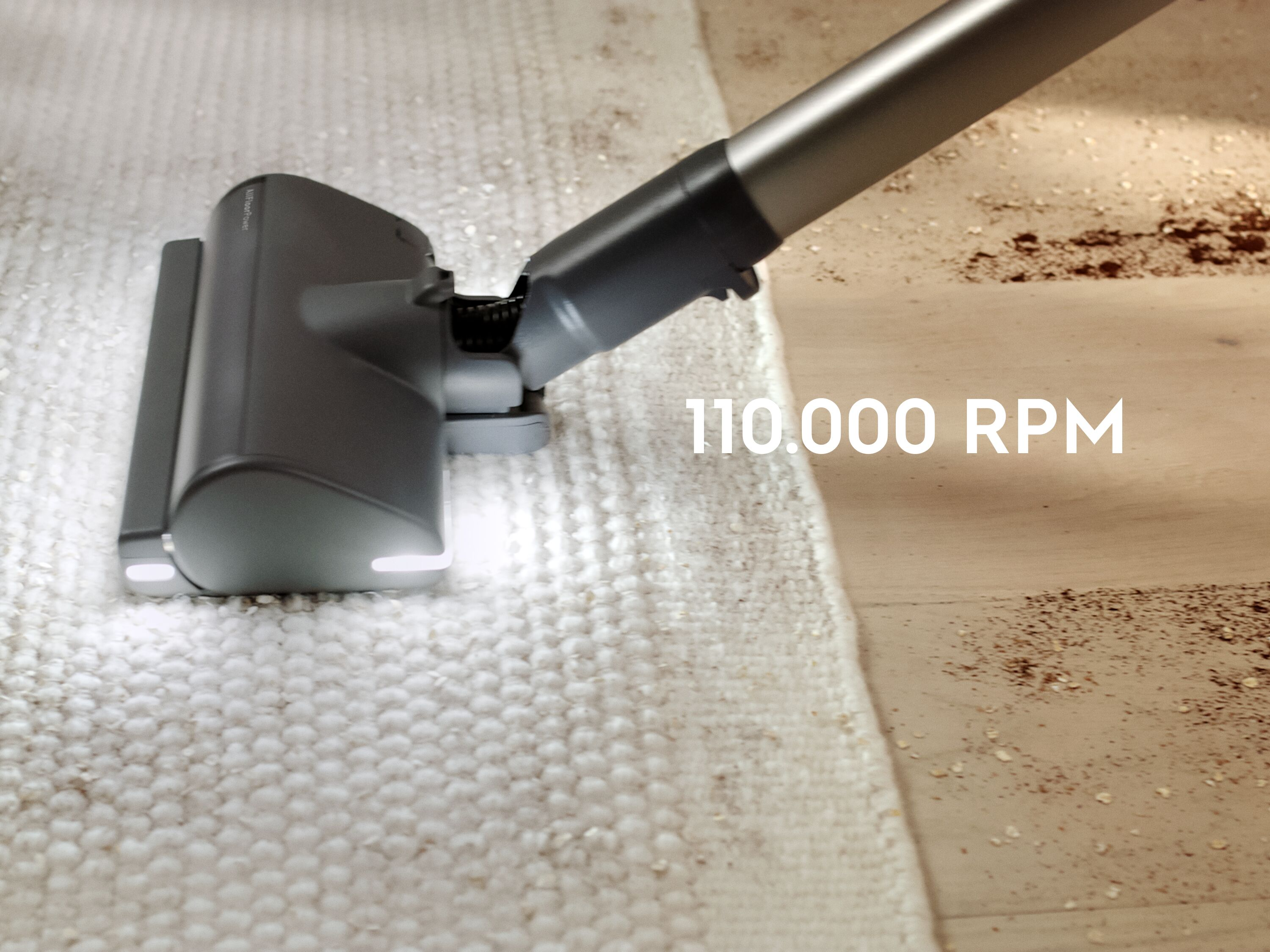 Ahşap bir zeminde açık renkli halıyı süpüren bir elektrikli süpürge ve 110.000 RPM yazısı.