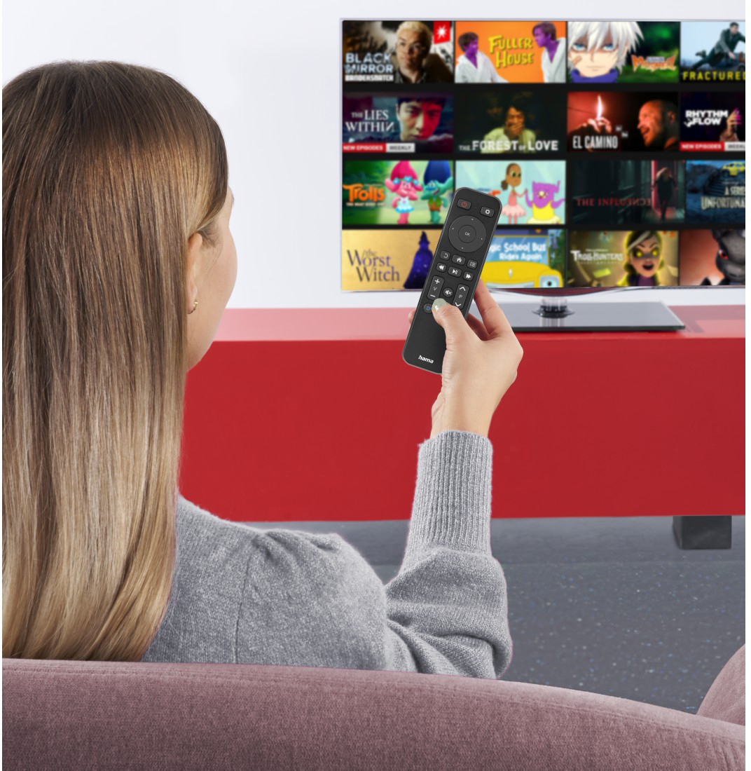Egy szőke nő egy kanin ül, távirányítót tart, és egy sok csatornás tévét néz.