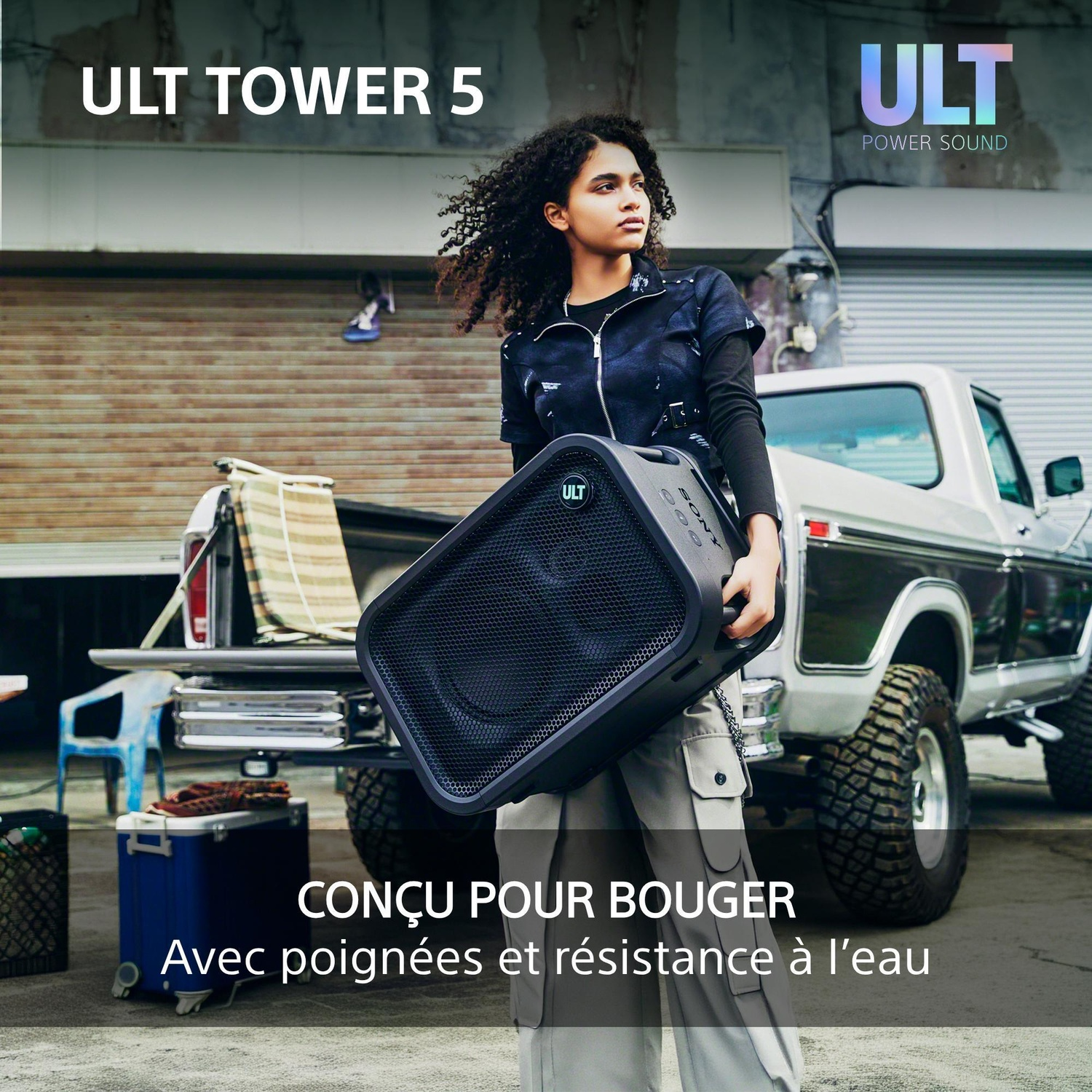 Une femme portant un grand haut-parleur noir devant une camionnette.