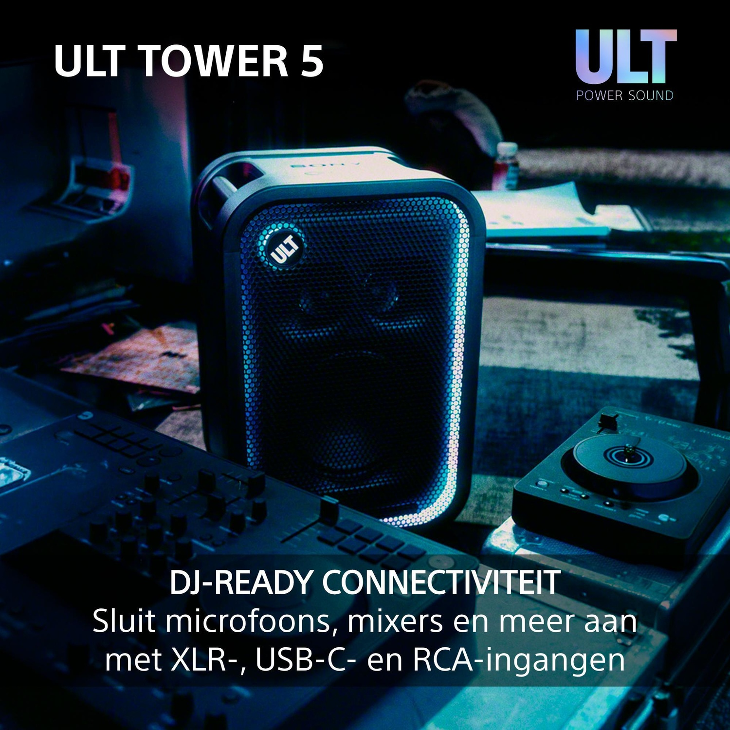 A black ULT Tower 5 speaker with blue lighting stands in a studio next to DJ equipment.