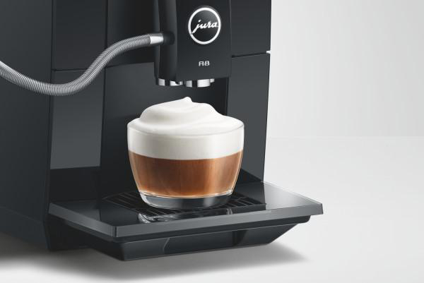Ein schwarzer Jura Kaffeevollautomat bereitet einen Cappuccino in einer Tasse mit dickem Milchschaum zu.