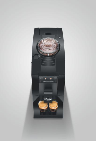 Schwarze Kaffeemaschine von oben mit sichtbaren Bohnen im Behälter und zwei Gläsern Espresso auf einer grauen Fläche.