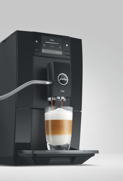 Eine schwarze Jura Kaffeemaschine brüht einen Latte Macchiato in ein Glas mit geschichteter Milch und Schaum.