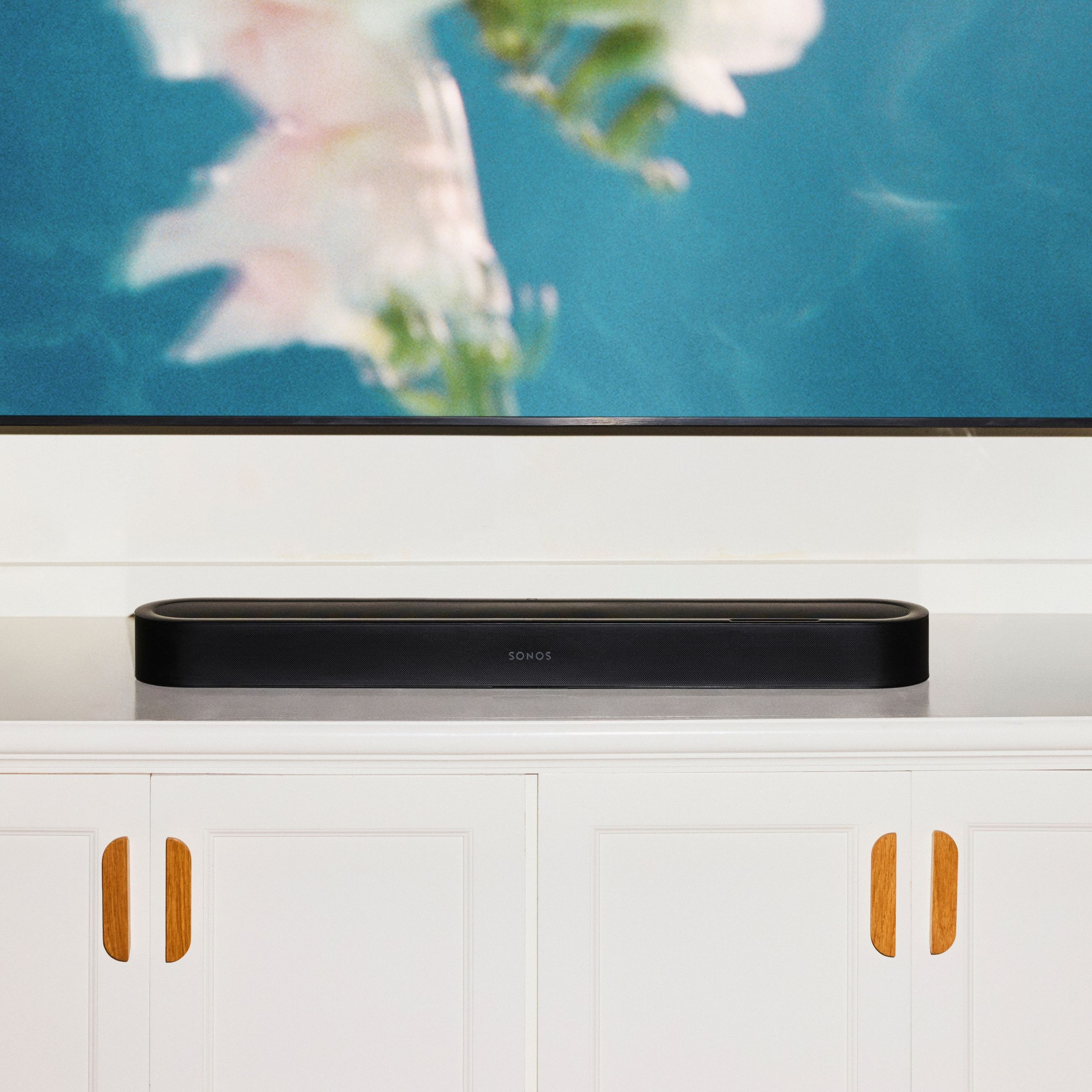 Une barre de son Sonos noire posée sur un meuble blanc sous une télévision.