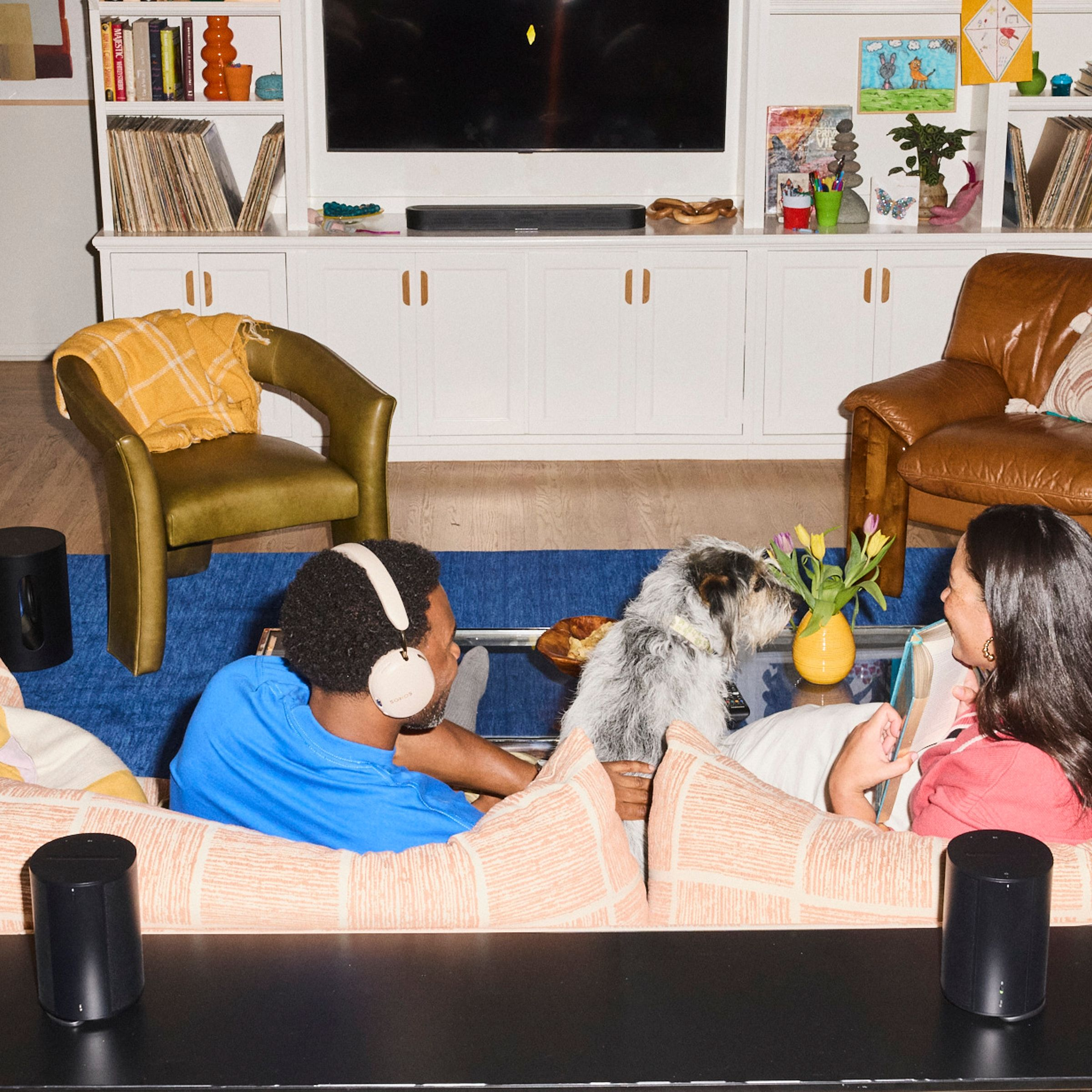 Un couple est assis dans un salon avec un chien, lisant un livre et portant un casque.