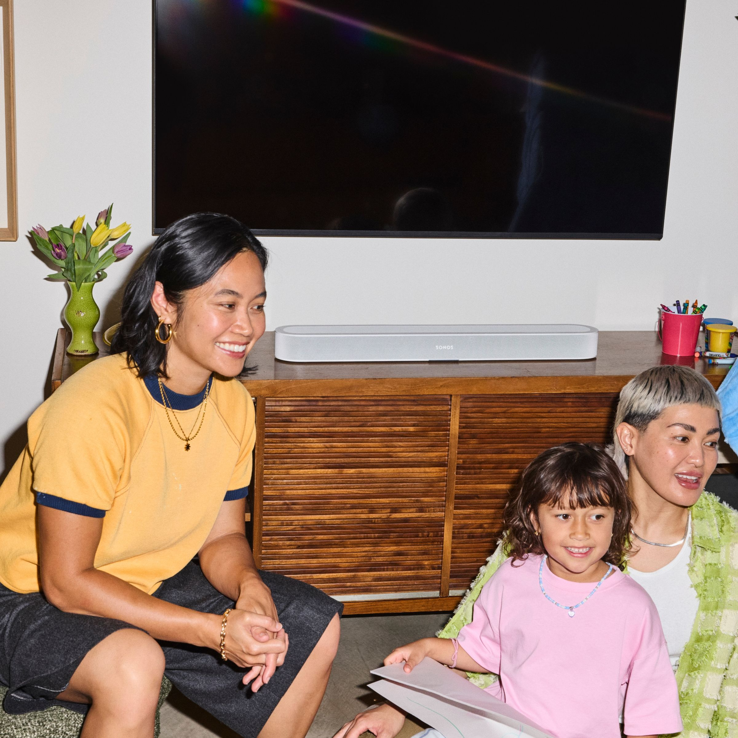 Deux femmes et un enfant sont assis ensemble dans un salon avec une télévision et un meuble.