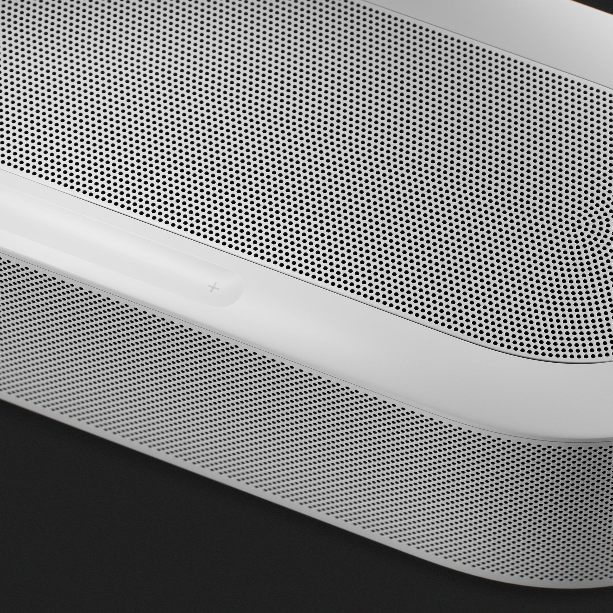 Gros plan d'un haut-parleur blanc avec grille perforée et bouton plus.