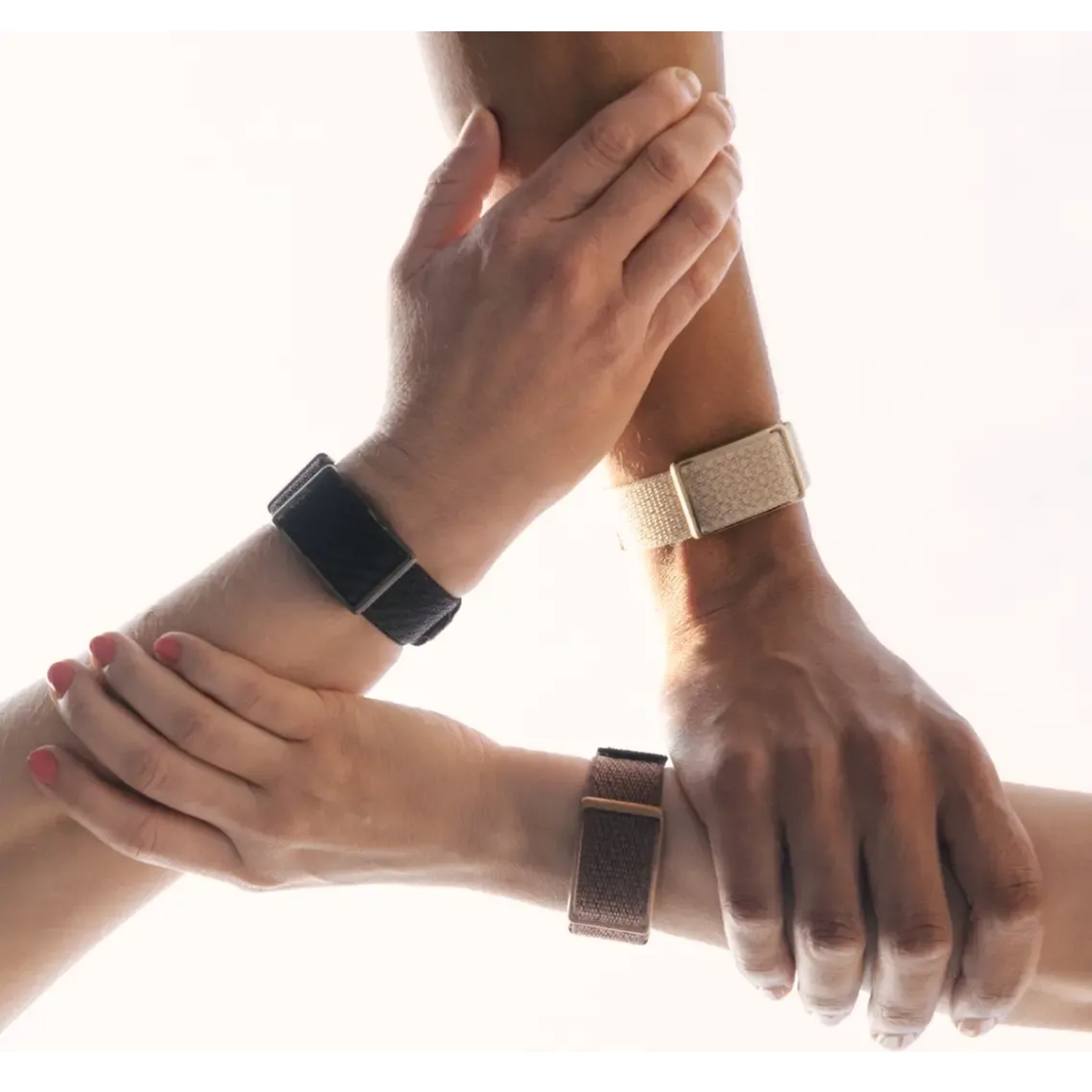 Three arms holding each other in a circle, each wearing a smartwatch on the wrist against a bright white background.