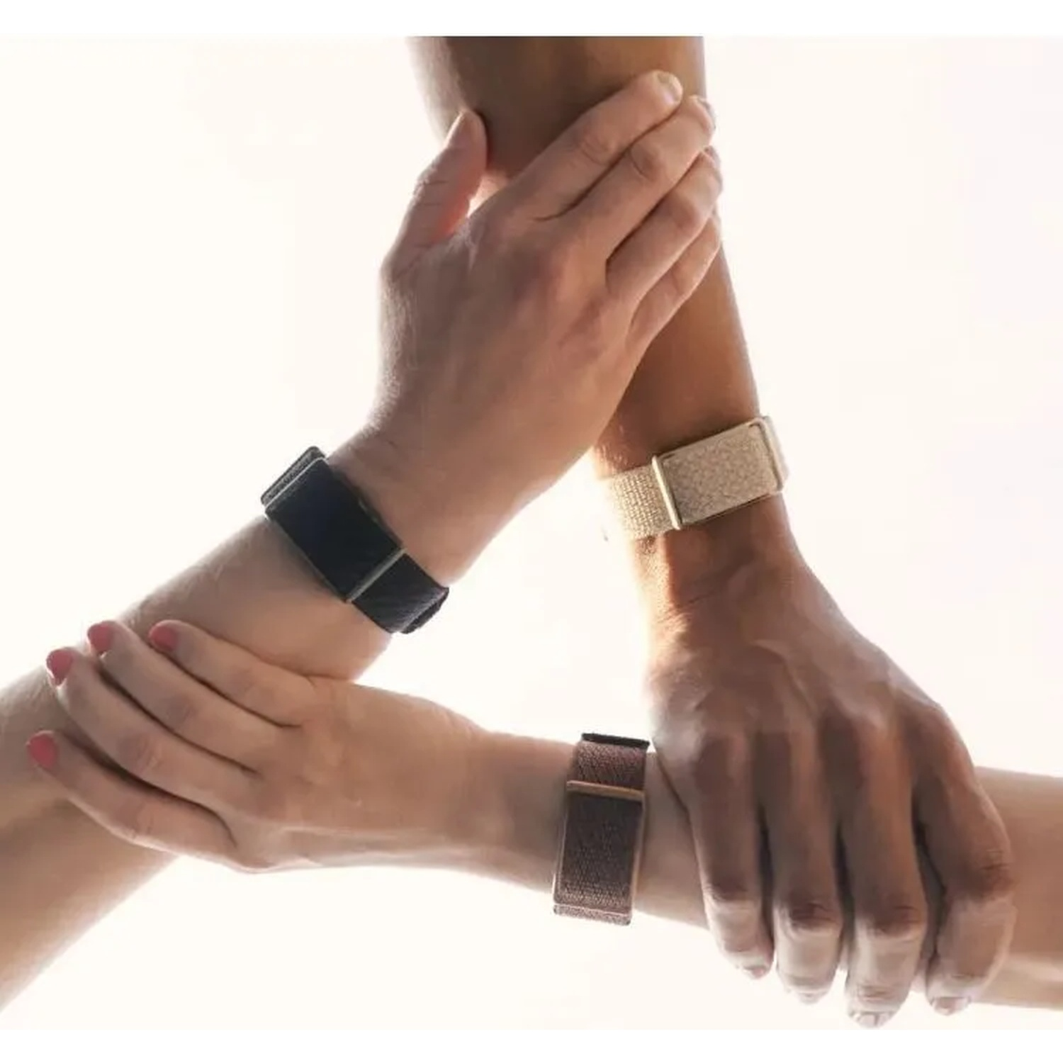 Three arms join in a circle, each wearing a smartwatch with different colored bands against a bright background.