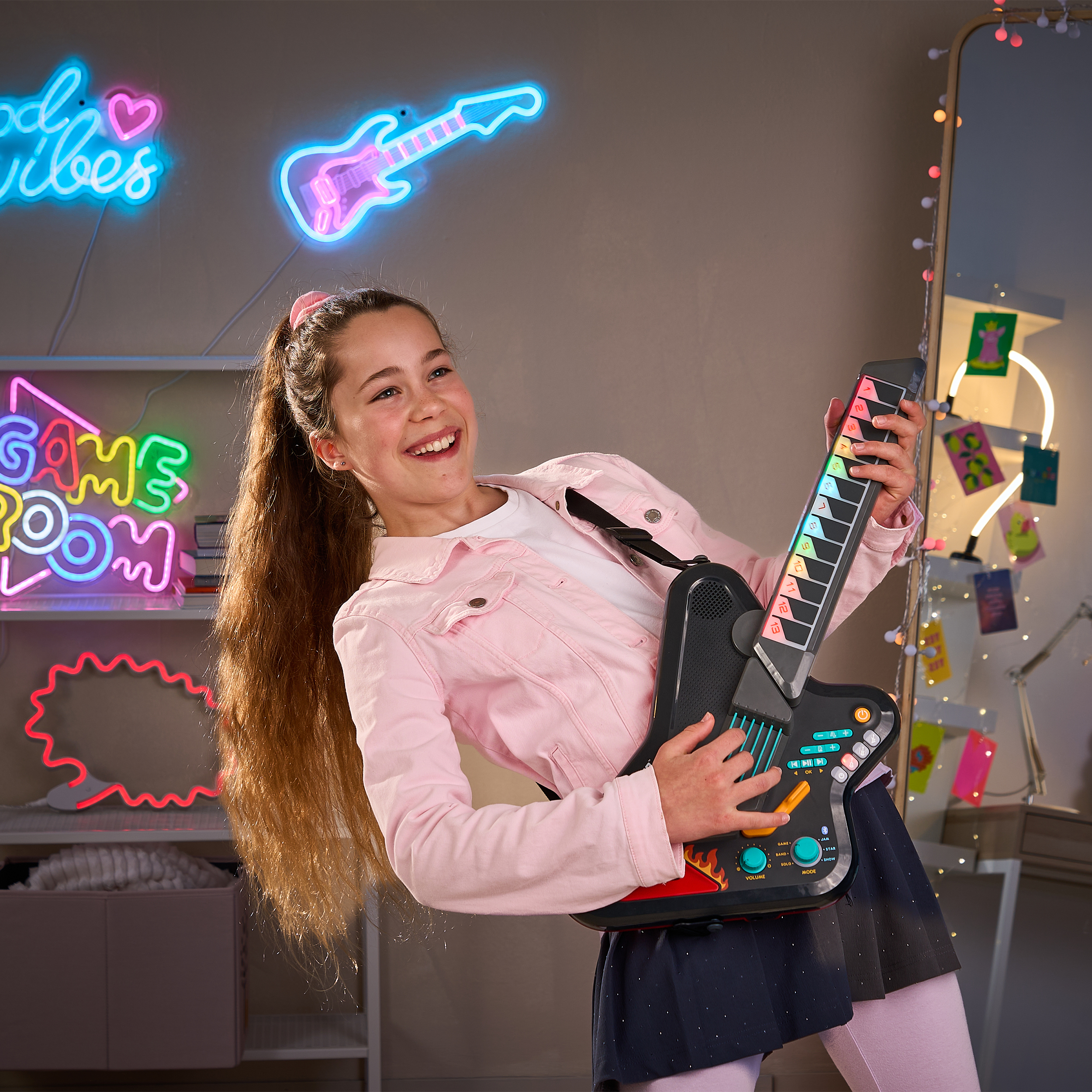 Ein glückliches Mädchen im pinken Jackett spielt drinnen Luftgitarre mit leuchtenden Neonlichtern im Hintergrund.