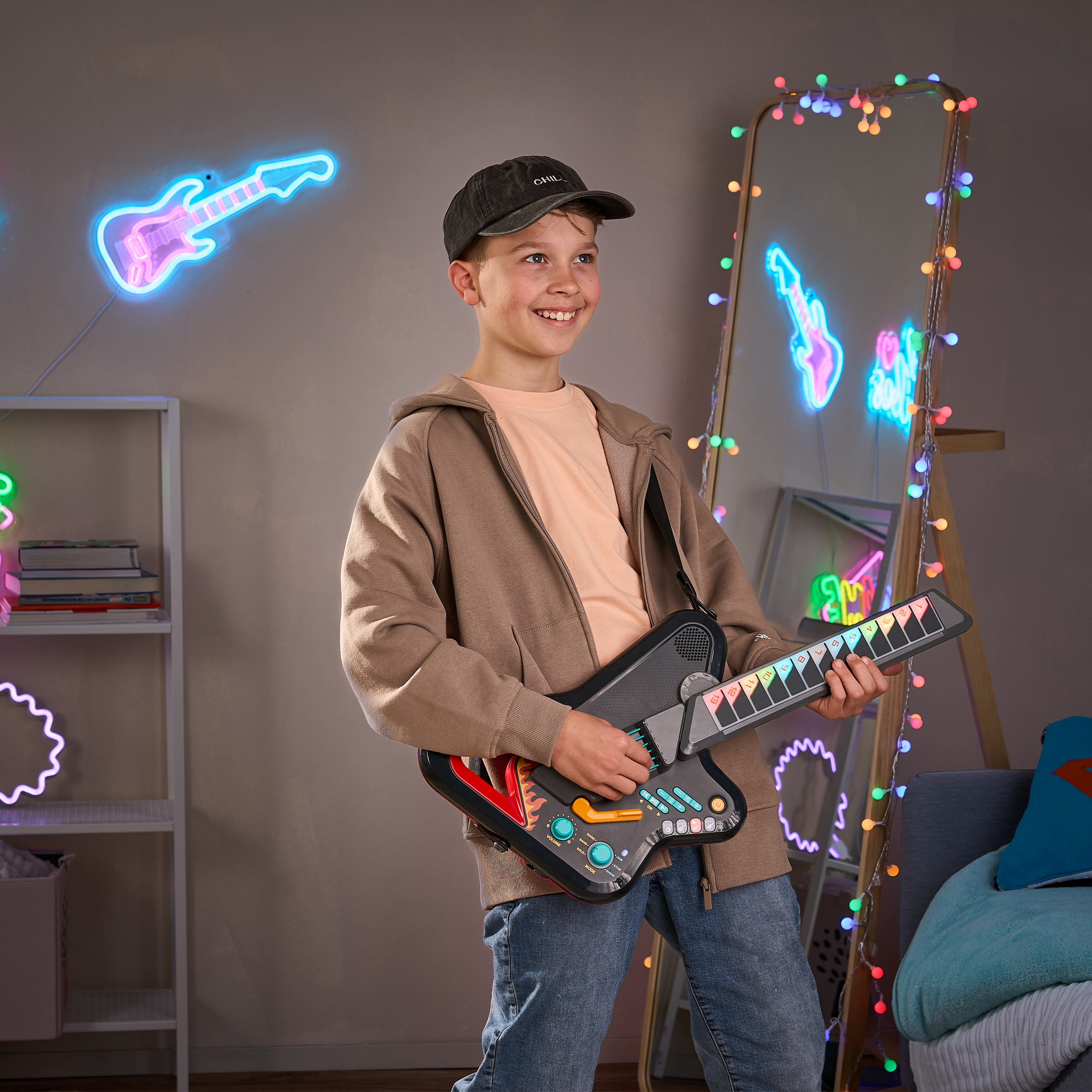 Ein Junge mit Mütze und braunem Hoodie lächelt und spielt Spielzeug-Gitarre in neonbeleuchtetem Raum.