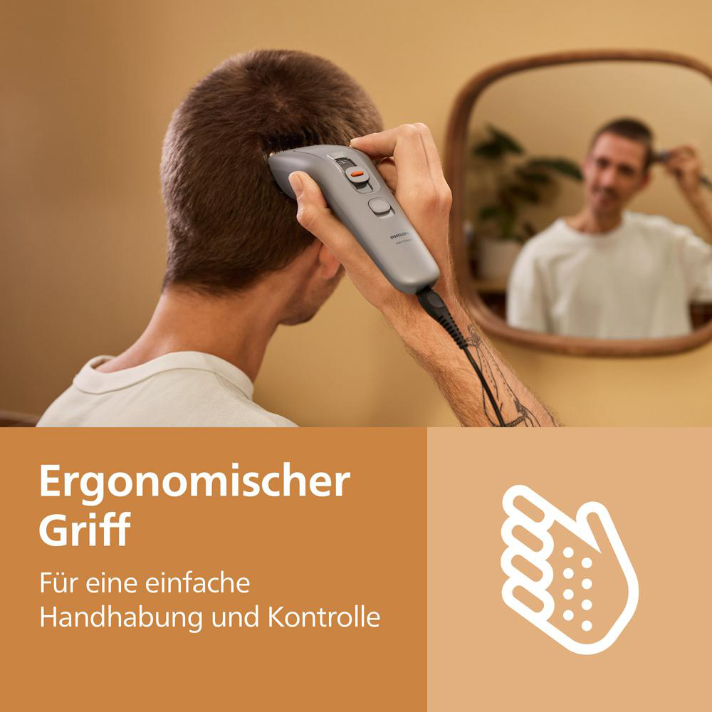 Ein Mann schneidet sich mit einem grauen Haarschneider die Haare, im Hintergrund spiegelt er sich in einem Spiegel.