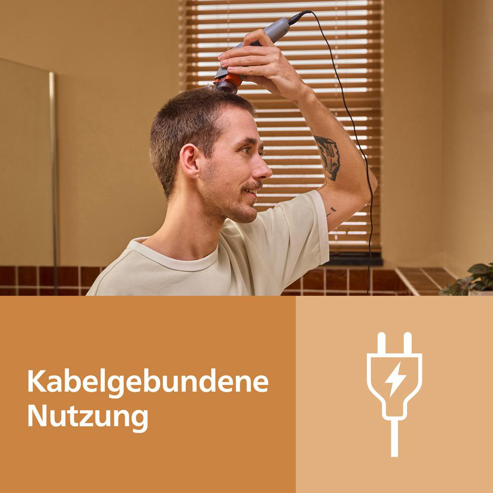 Ein Mann rasiert sich mit einem kabelgebundenen Rasierer vor einem Fenster mit Jalousien.