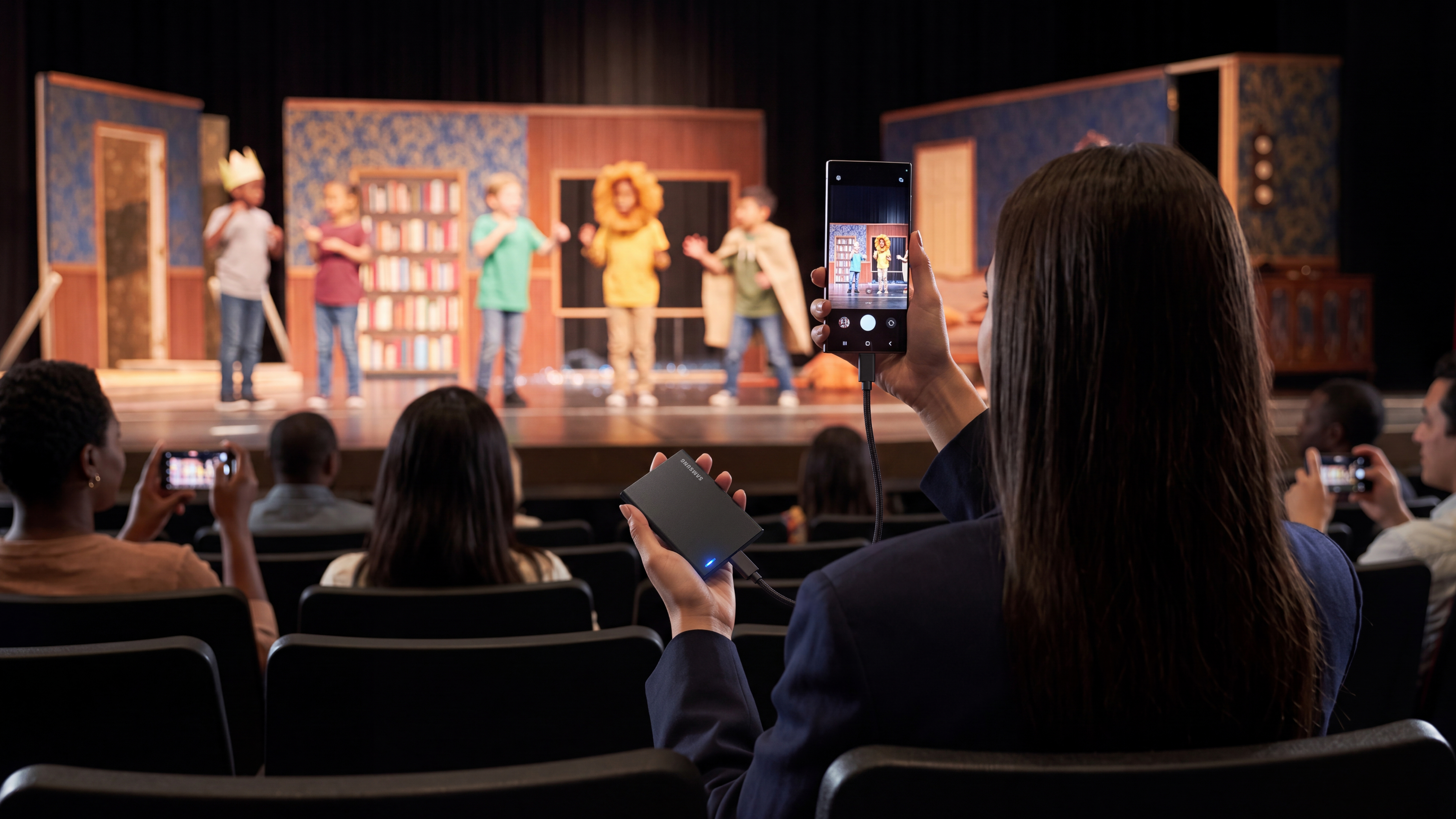 Eine Frau im Publikum filmt eine Schultheateraufführung mit ihrem Smartphone.